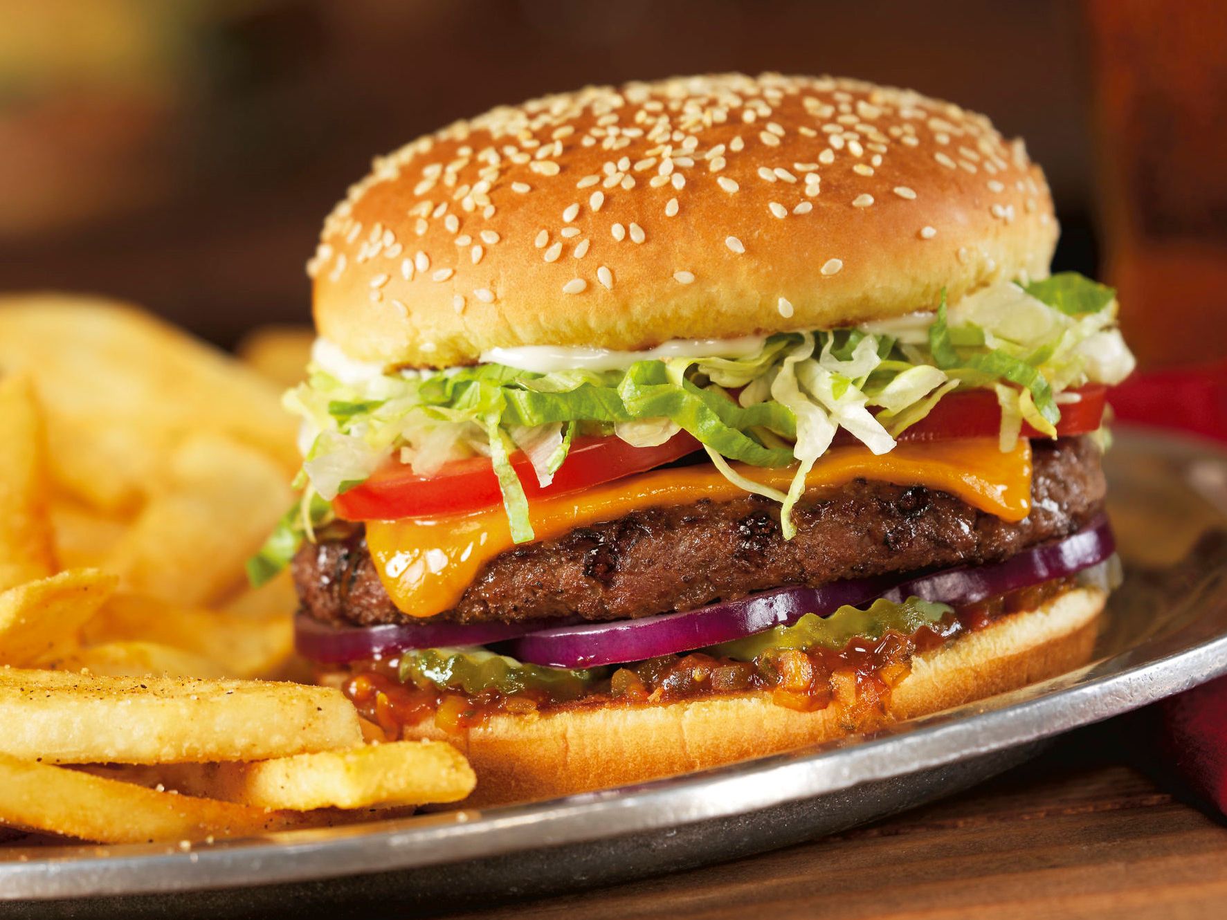 Cheeseburger with lettuce, tomato, onions, cheese, and fries on a plate