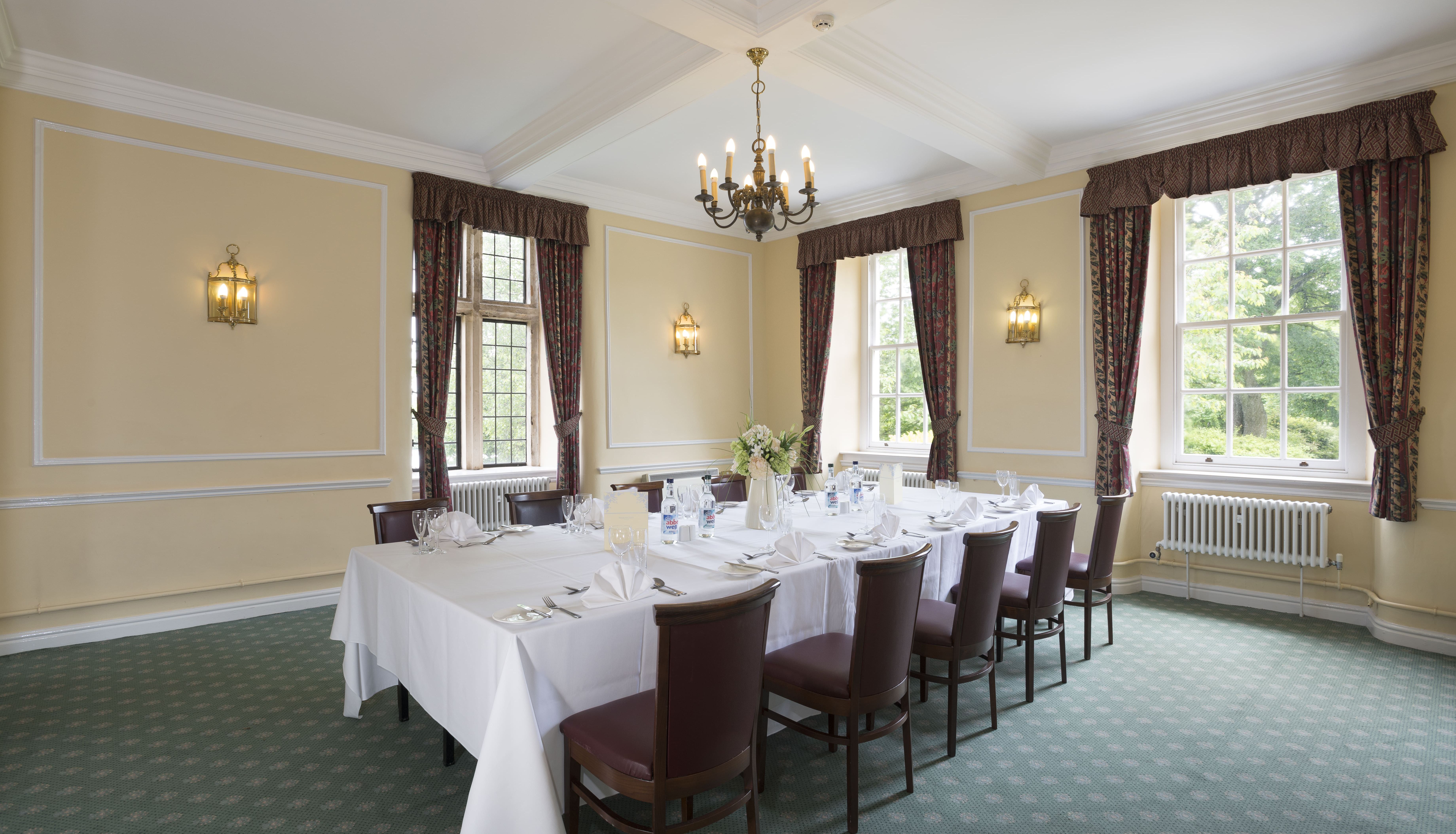 Elegant dining room with a set banquet table, surrounded by chairs and large windows with drapes.