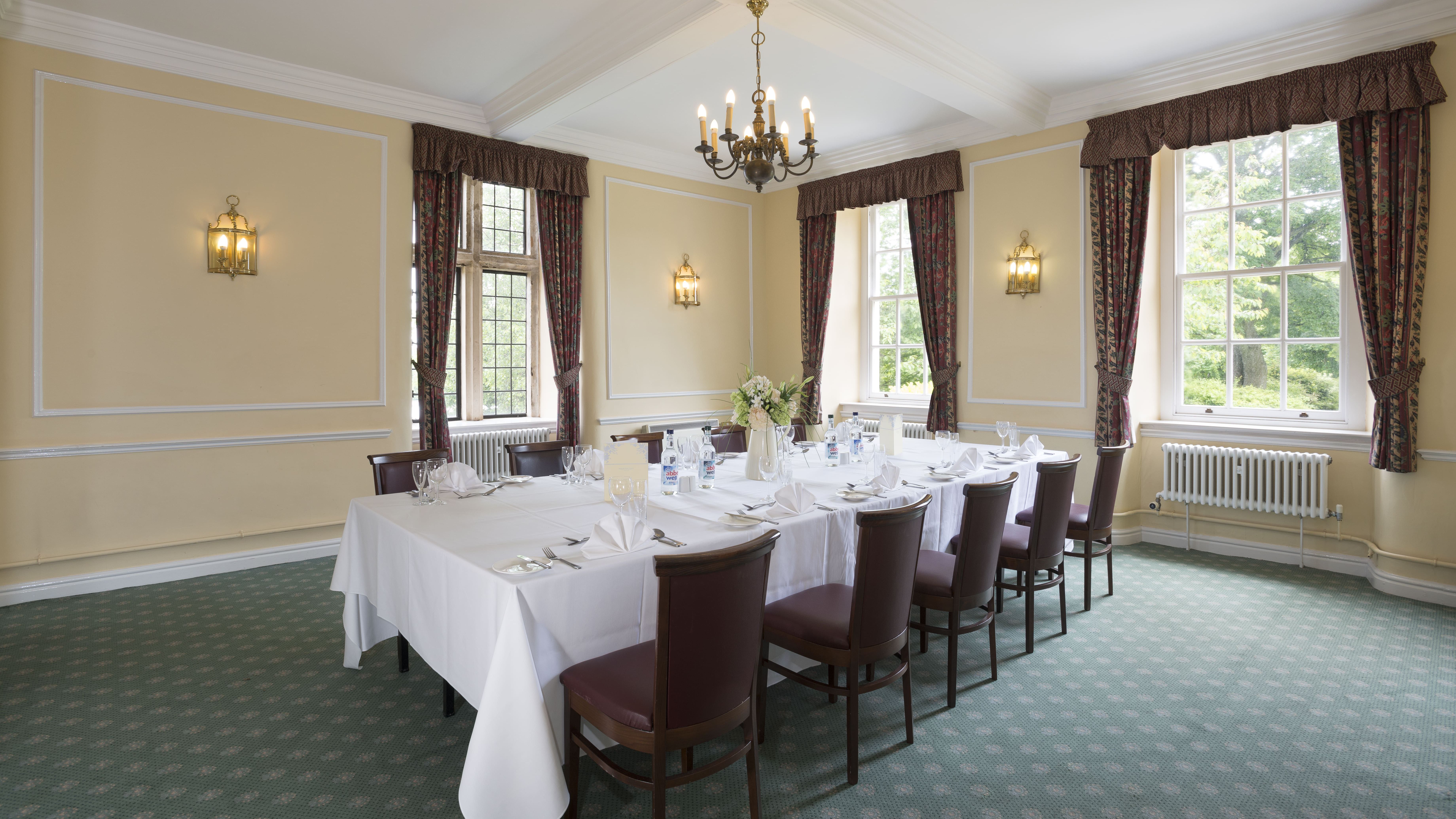 Elegant dining room with a set banquet table, surrounded by chairs and large windows with drapes.
