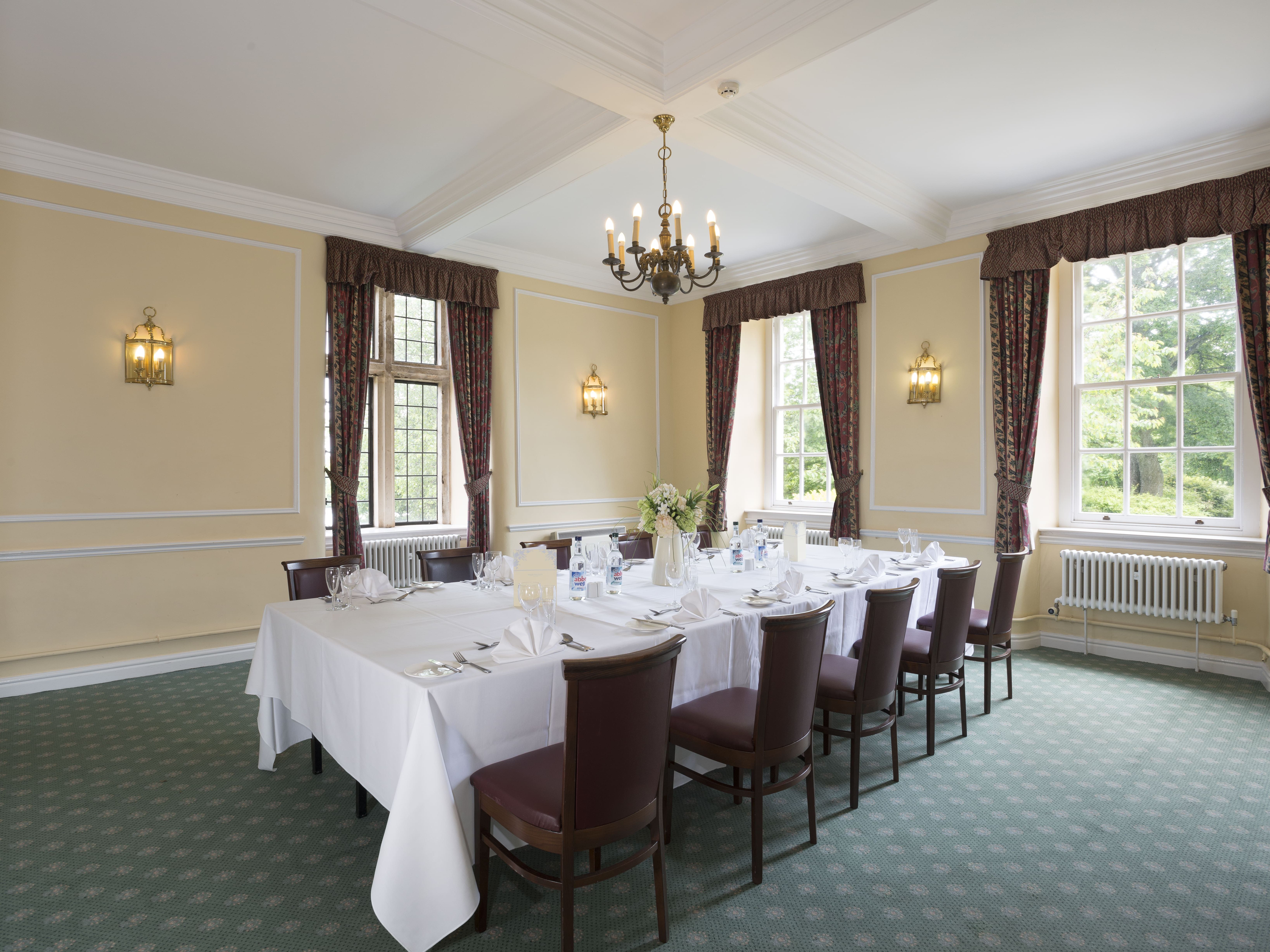 Elegant dining room with a set banquet table, surrounded by chairs and large windows with drapes.