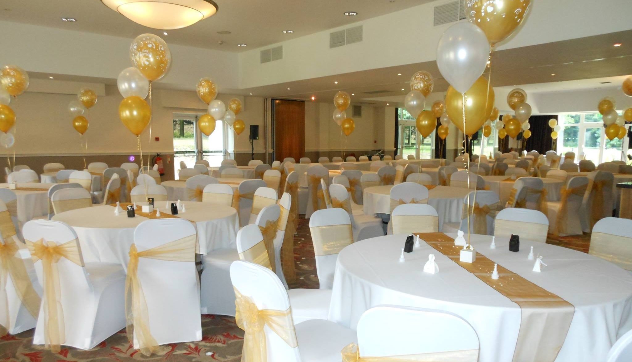 Elegant banquet hall decorated with gold and white balloons and chair covers