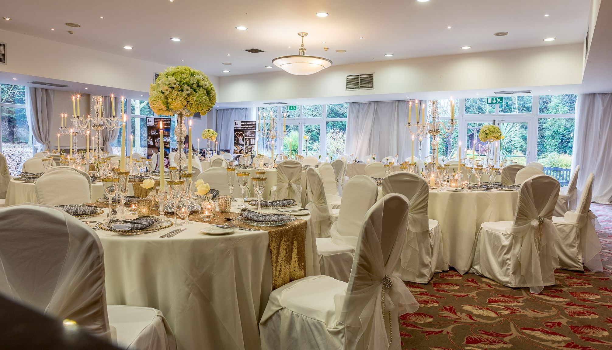 Elegant banquet hall set up for a wedding with round tables, white chair covers, and gold decorations.
