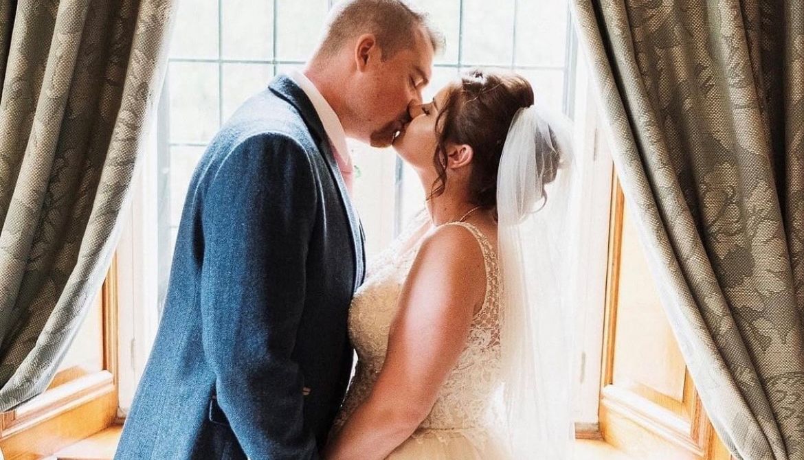 Bride and groom kissing in front of a window with curtains