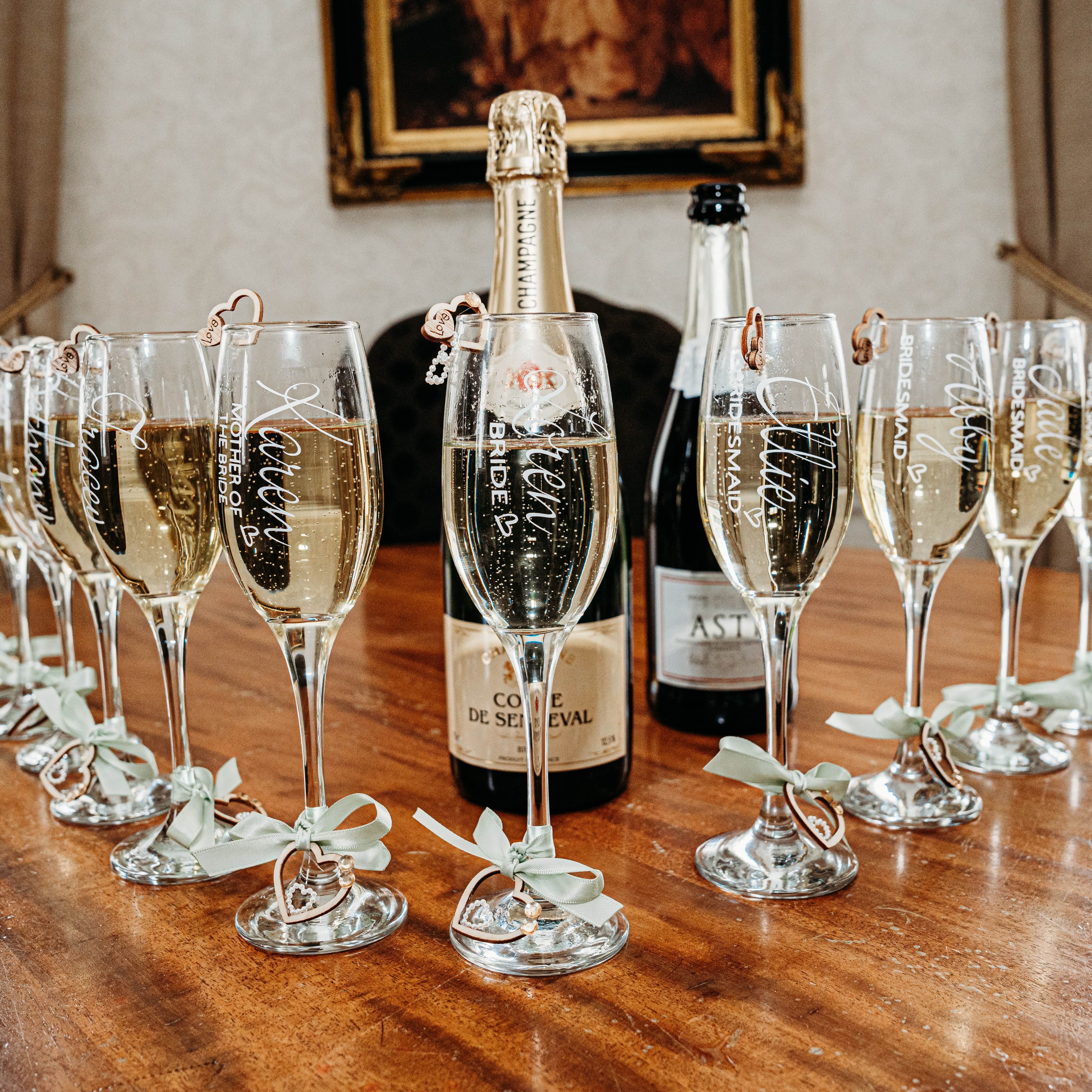 Champagne flutes with personalized names and titles arranged around champagne bottles on a wooden table.