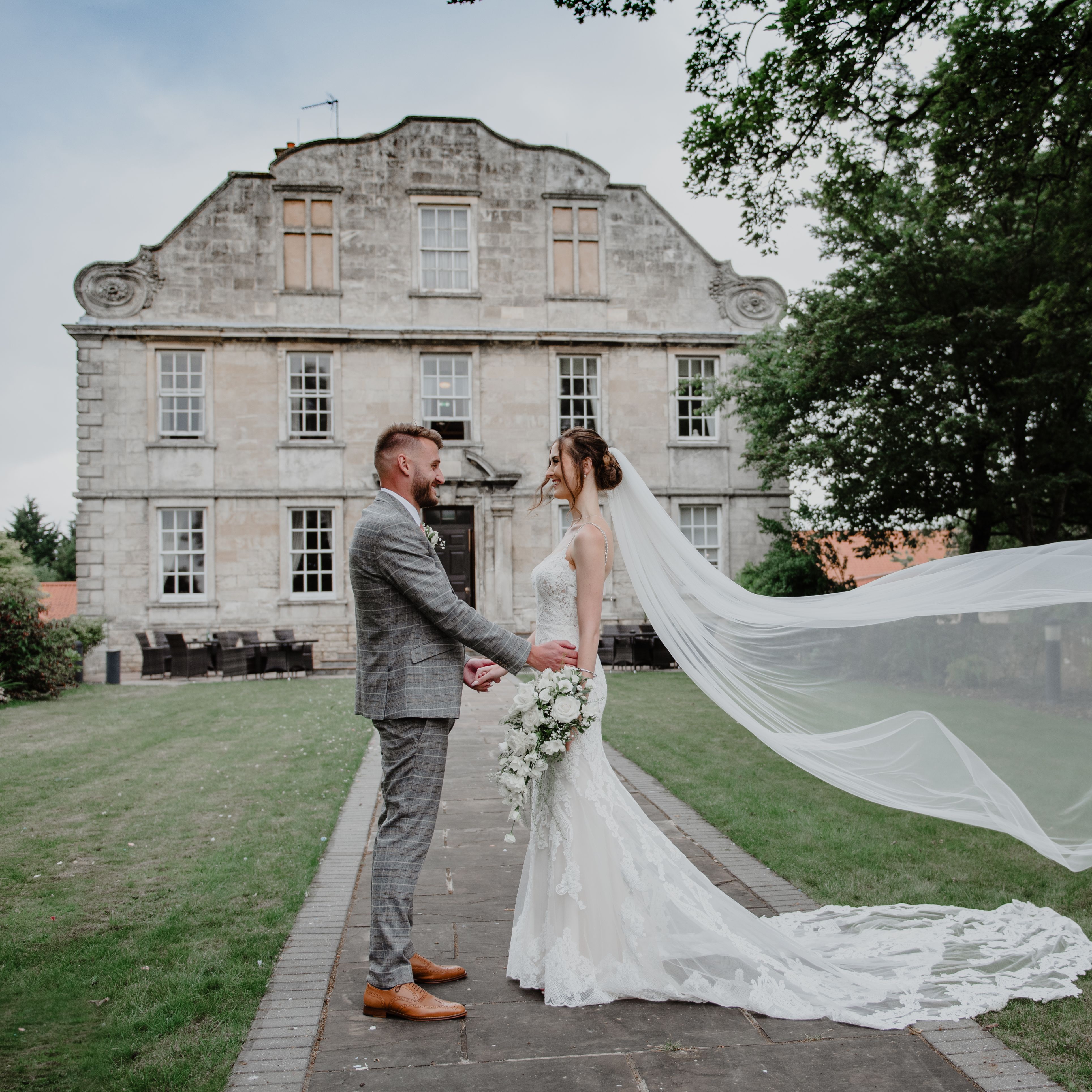 Bride and groom holding hands outside a historic building with the bride's veil flowing in the wind