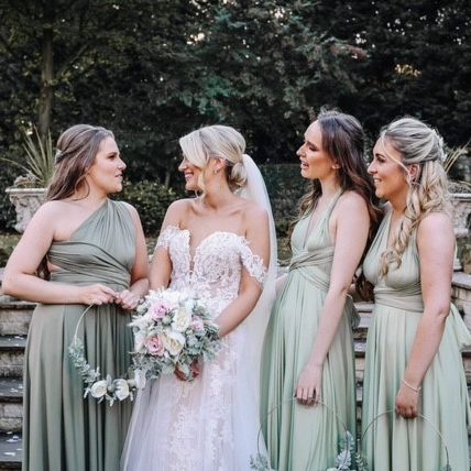 Bride in white dress standing with three bridesmaids in green dresses outdoors.