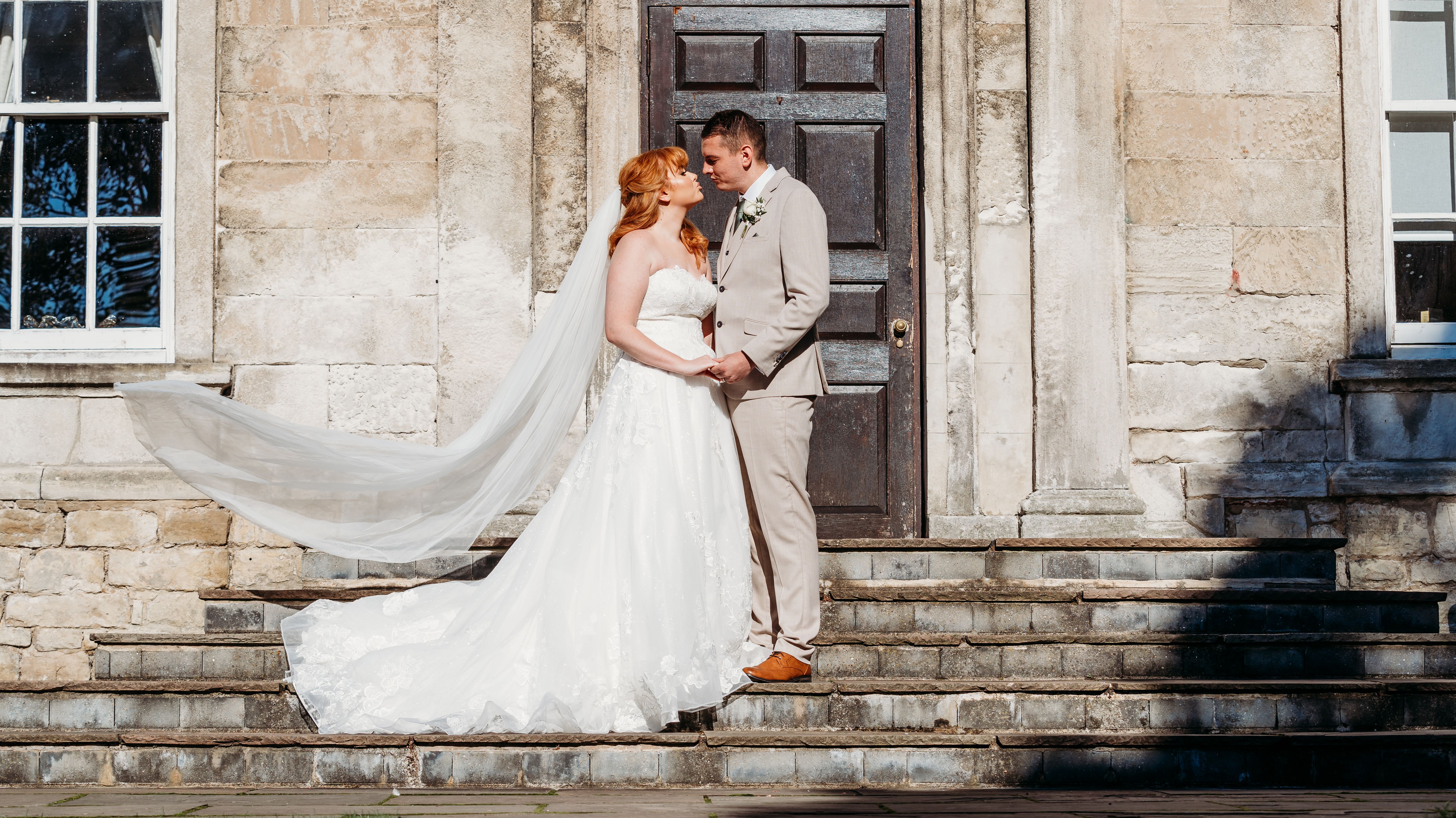 Bride and groom standing together on stone steps outside a historic building.