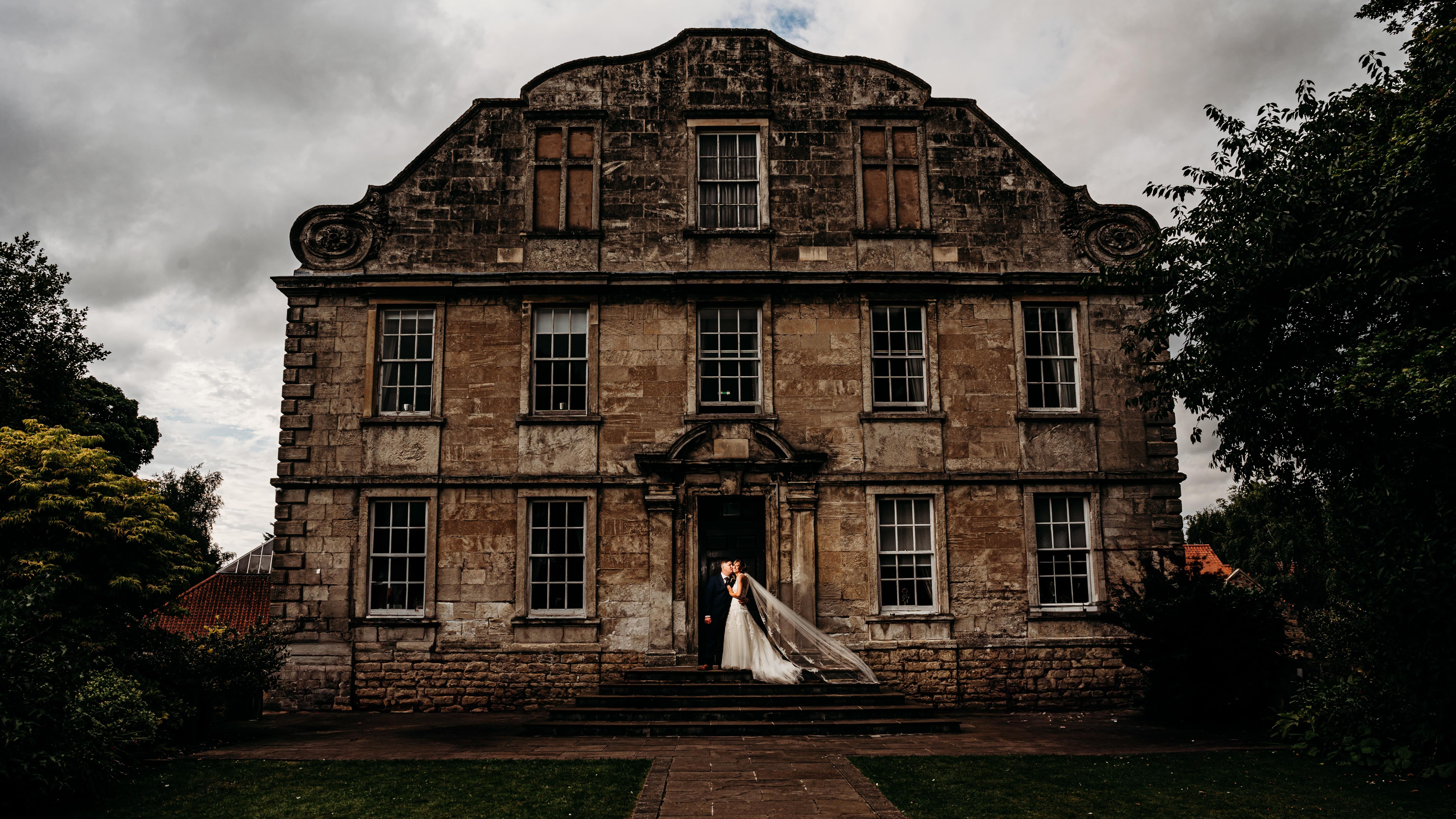 Bride and groom stand together outside a large historic stone building