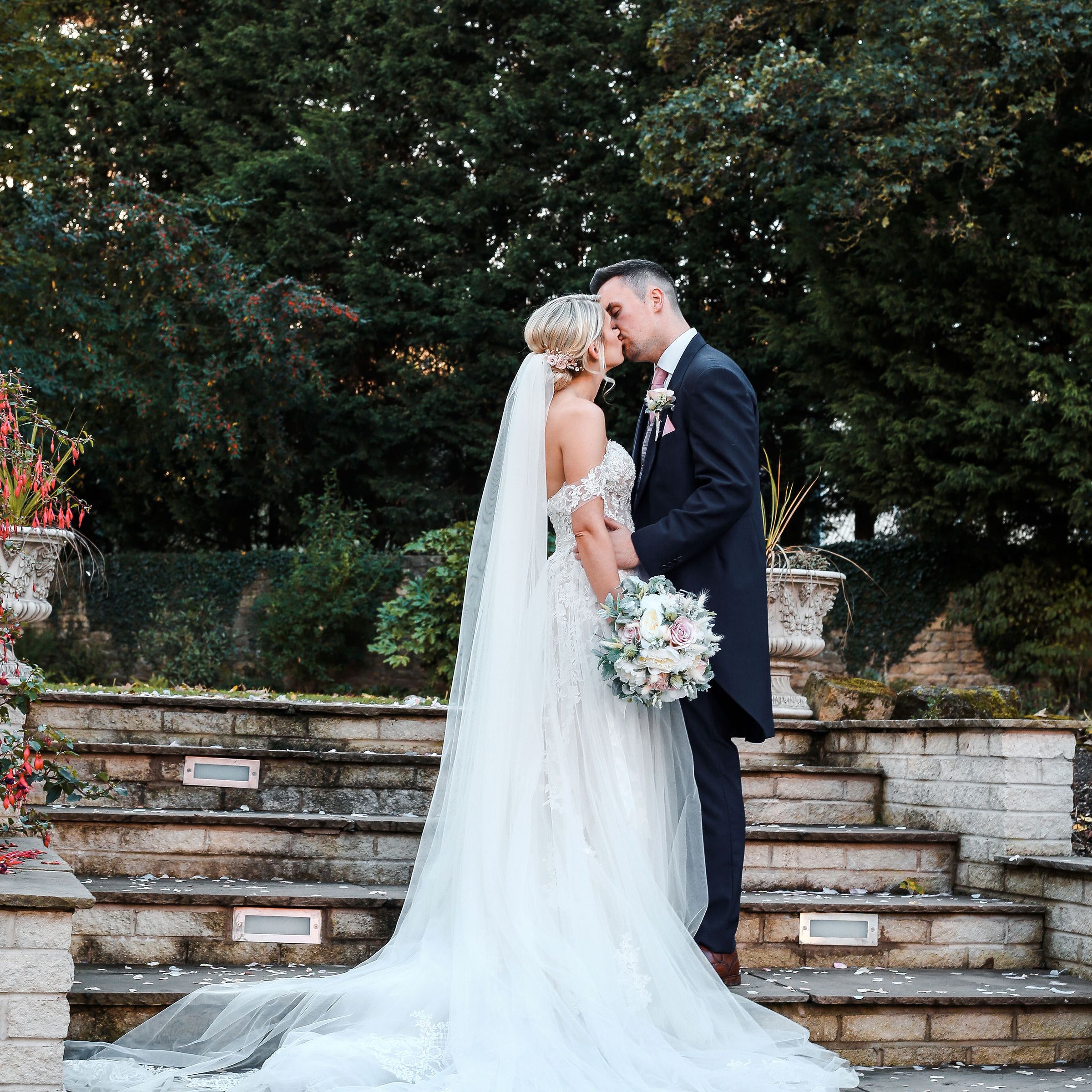 Bride and groom kissing on outdoor stone steps surrounded by greenery