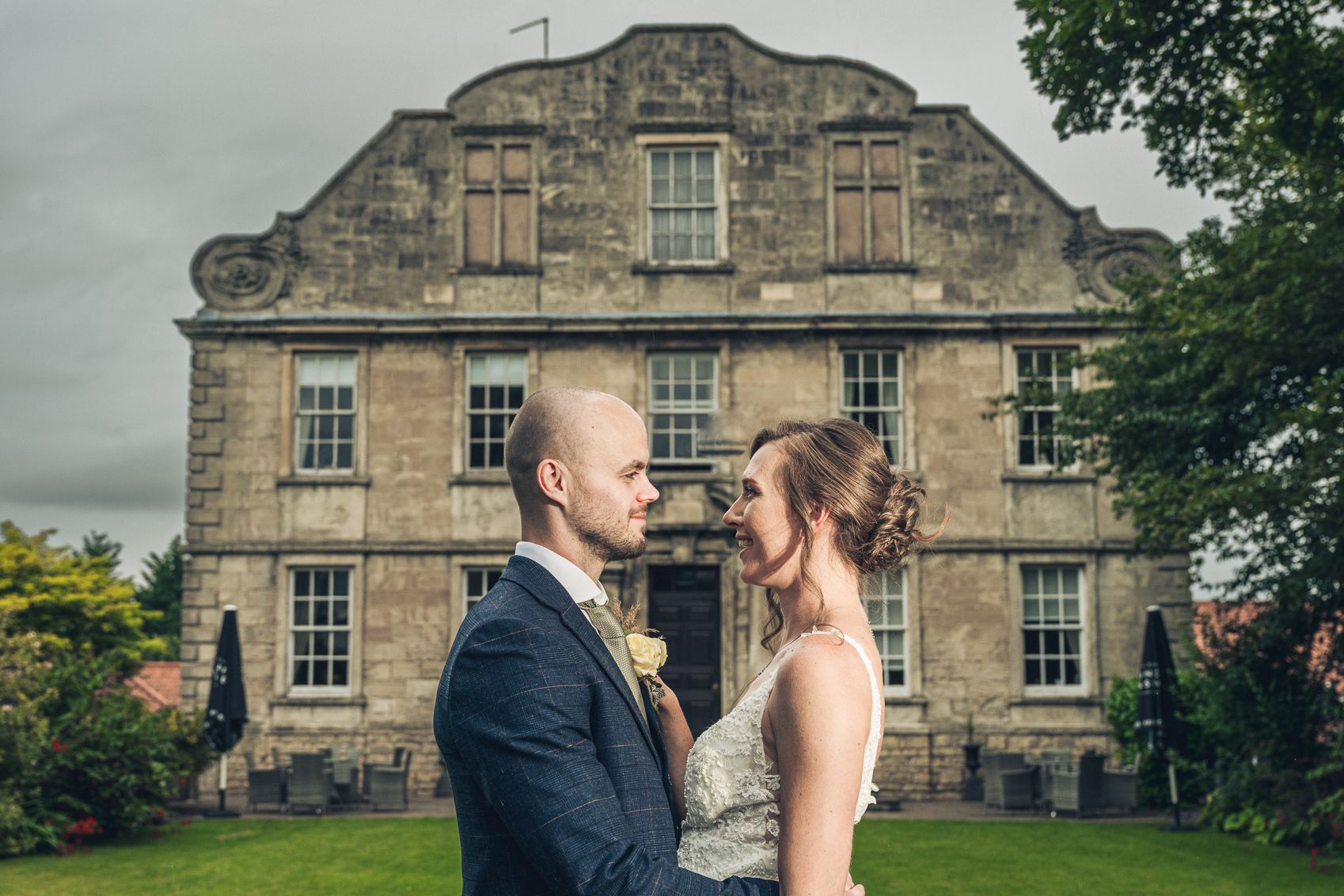 Bride and groom embrace in front of a historic stone building on their wedding day.