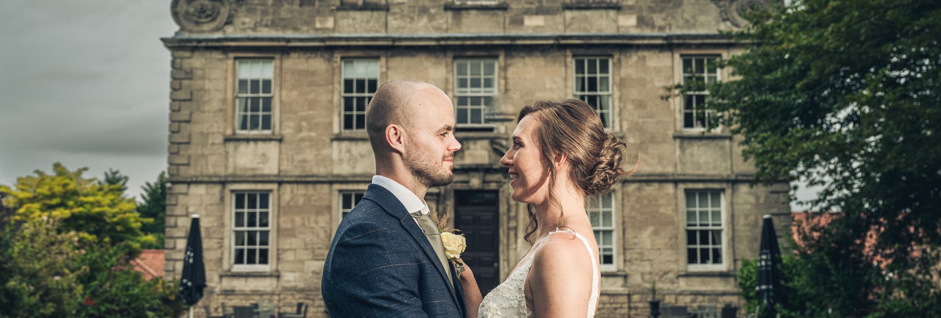 Bride and groom embrace in front of a historic stone building on their wedding day.