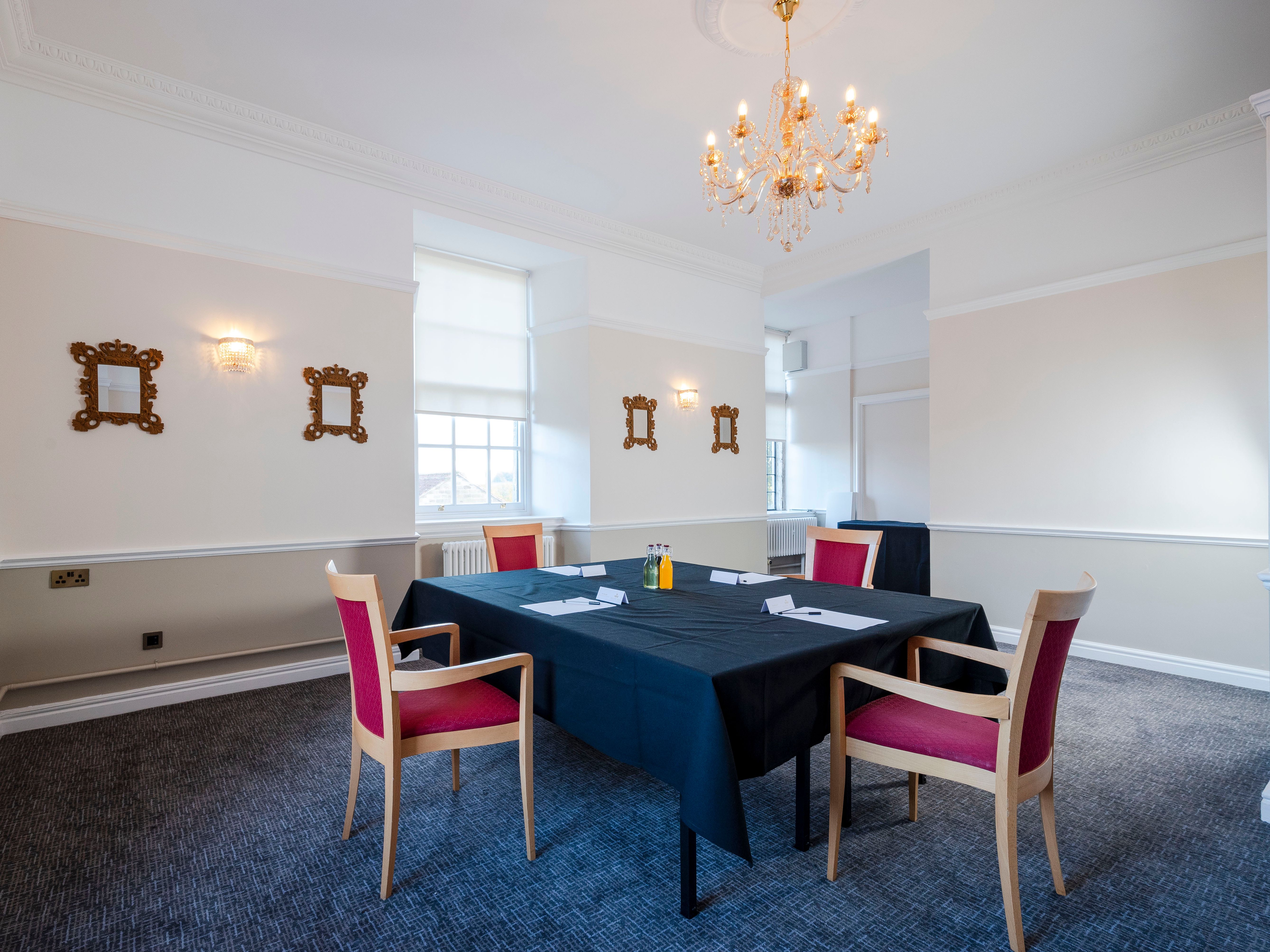 Meeting room with a black tablecloth, red chairs, chandeliers, and ornate wall mirrors