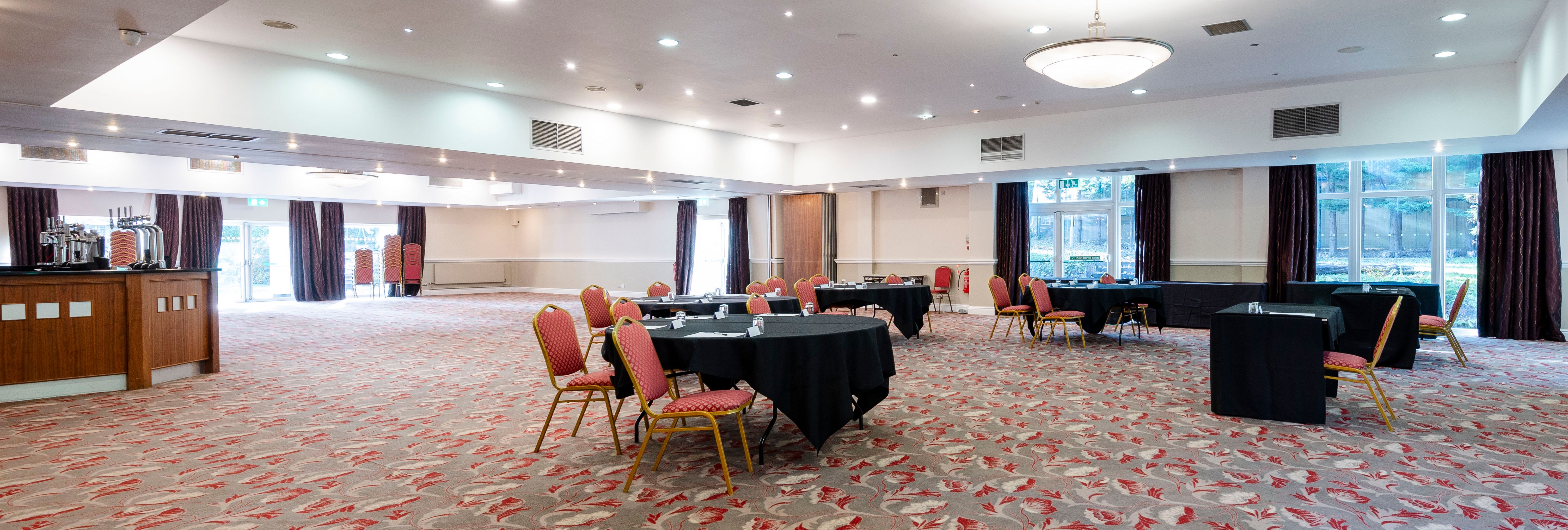 Spacious conference room with round tables and red chairs on a patterned carpet