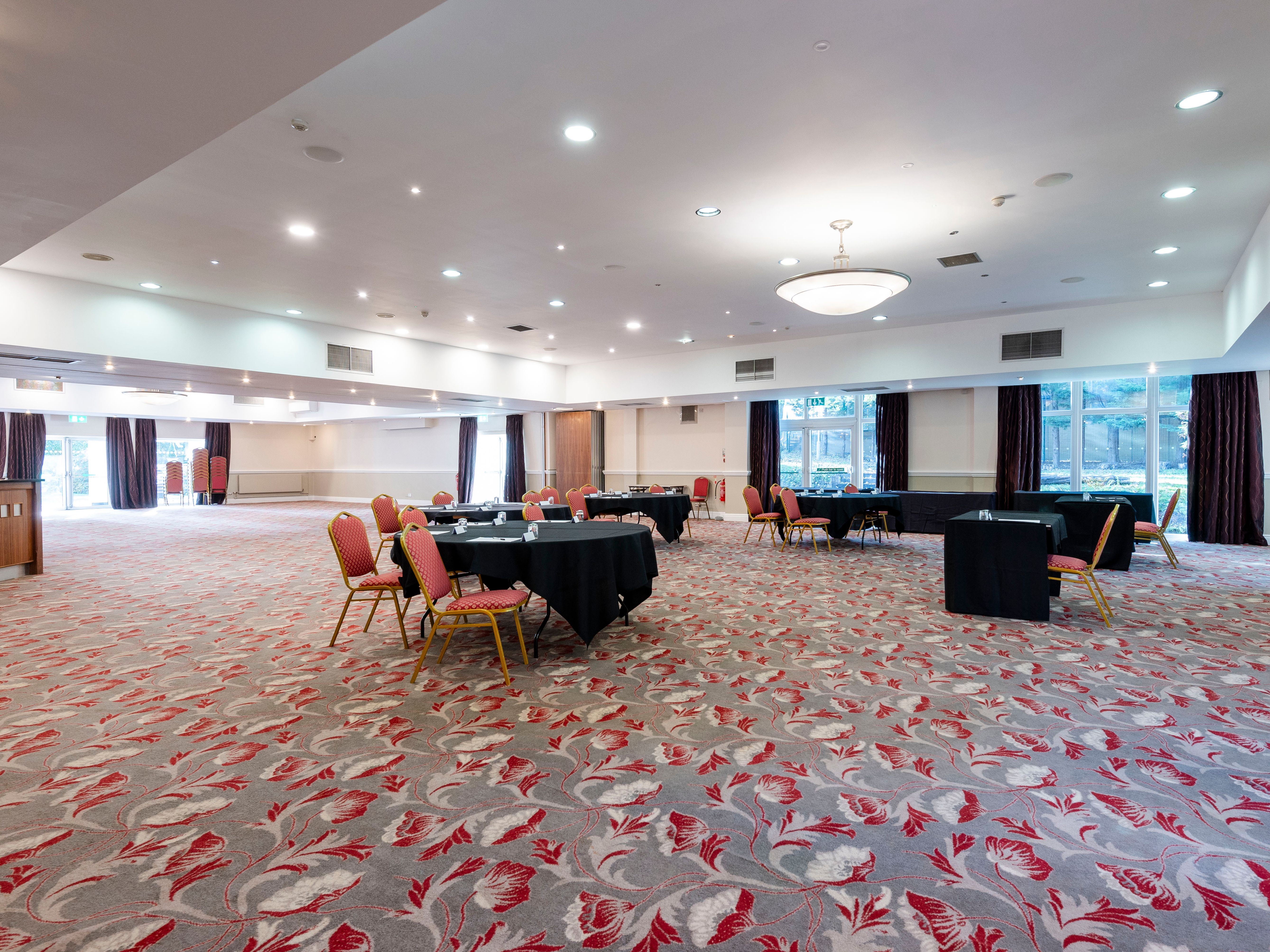 Spacious conference room with round tables and red chairs on a patterned carpet
