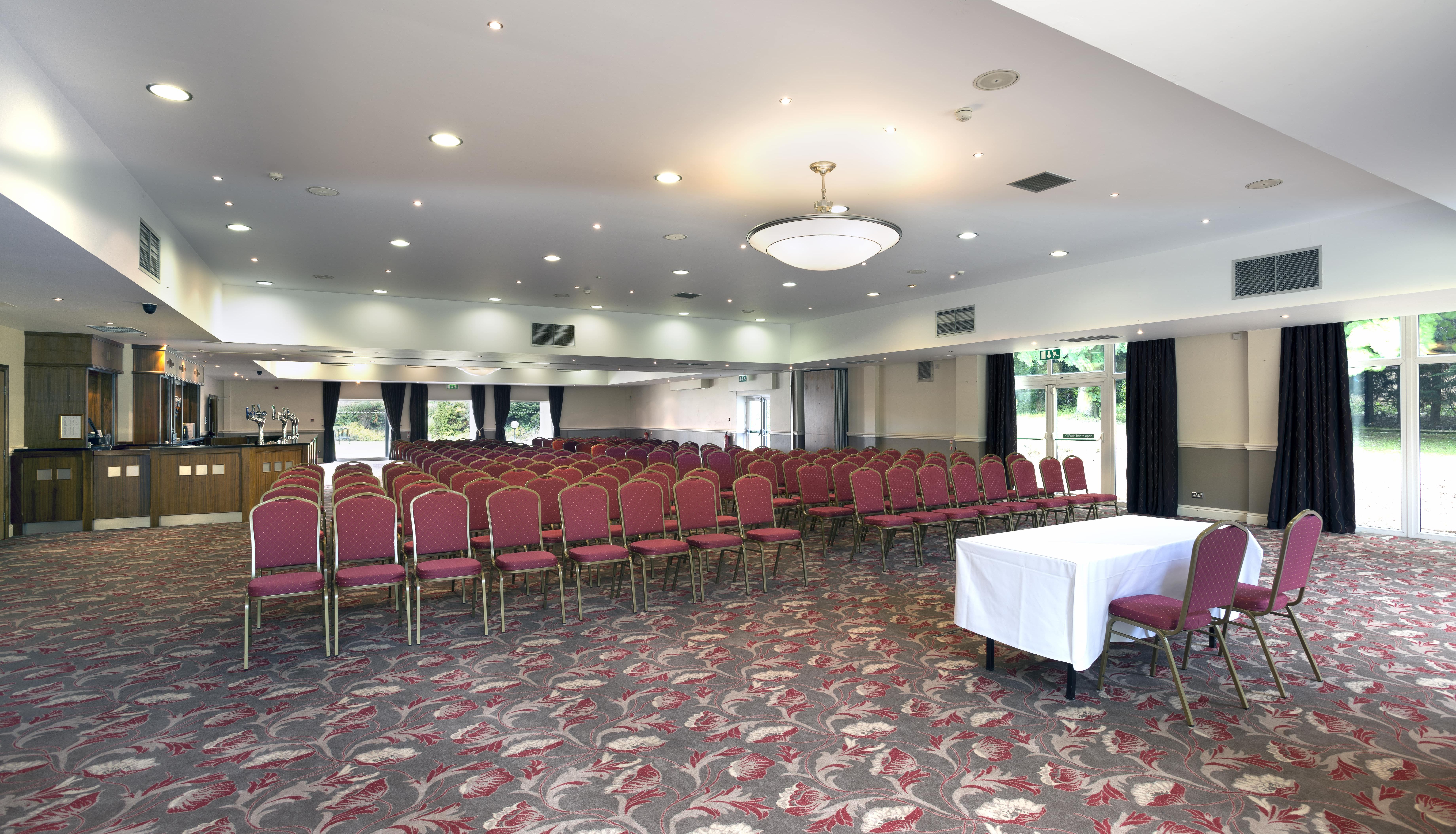 Empty conference room with rows of red chairs, a white table at the front, and patterned carpet
