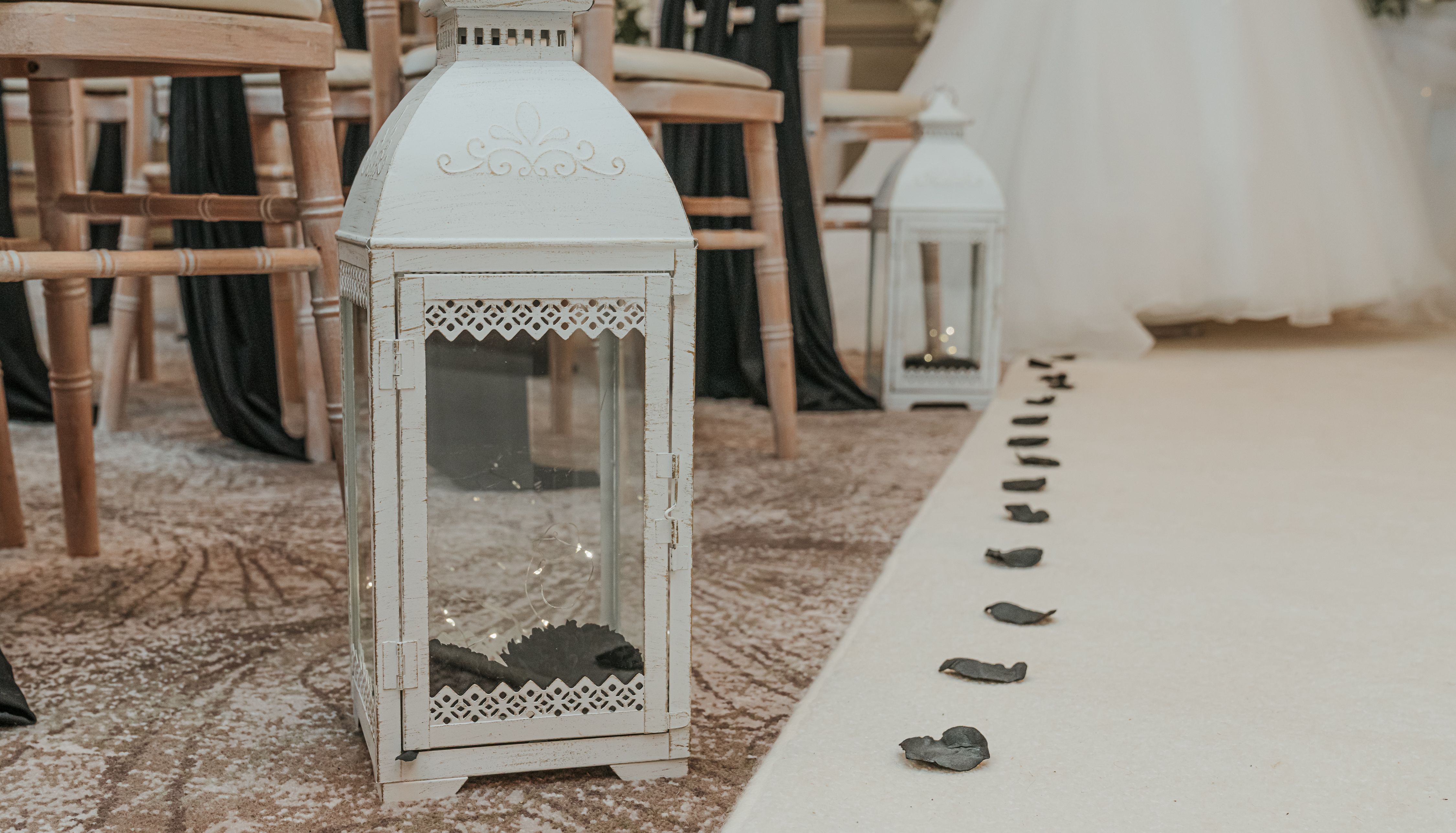White decorative lanterns and scattered black rose petals lining an aisle at a wedding ceremony.