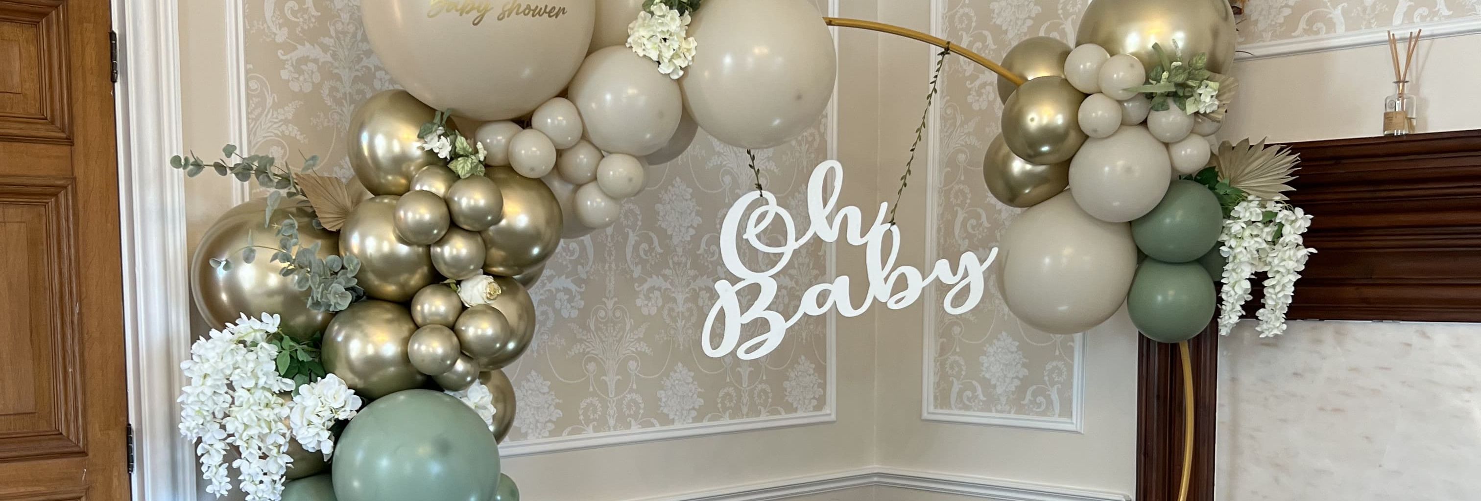 Elegant baby shower setup with pastel balloons, teddy bears, flowers, a wicker basket, and an 'Oh Baby' sign.