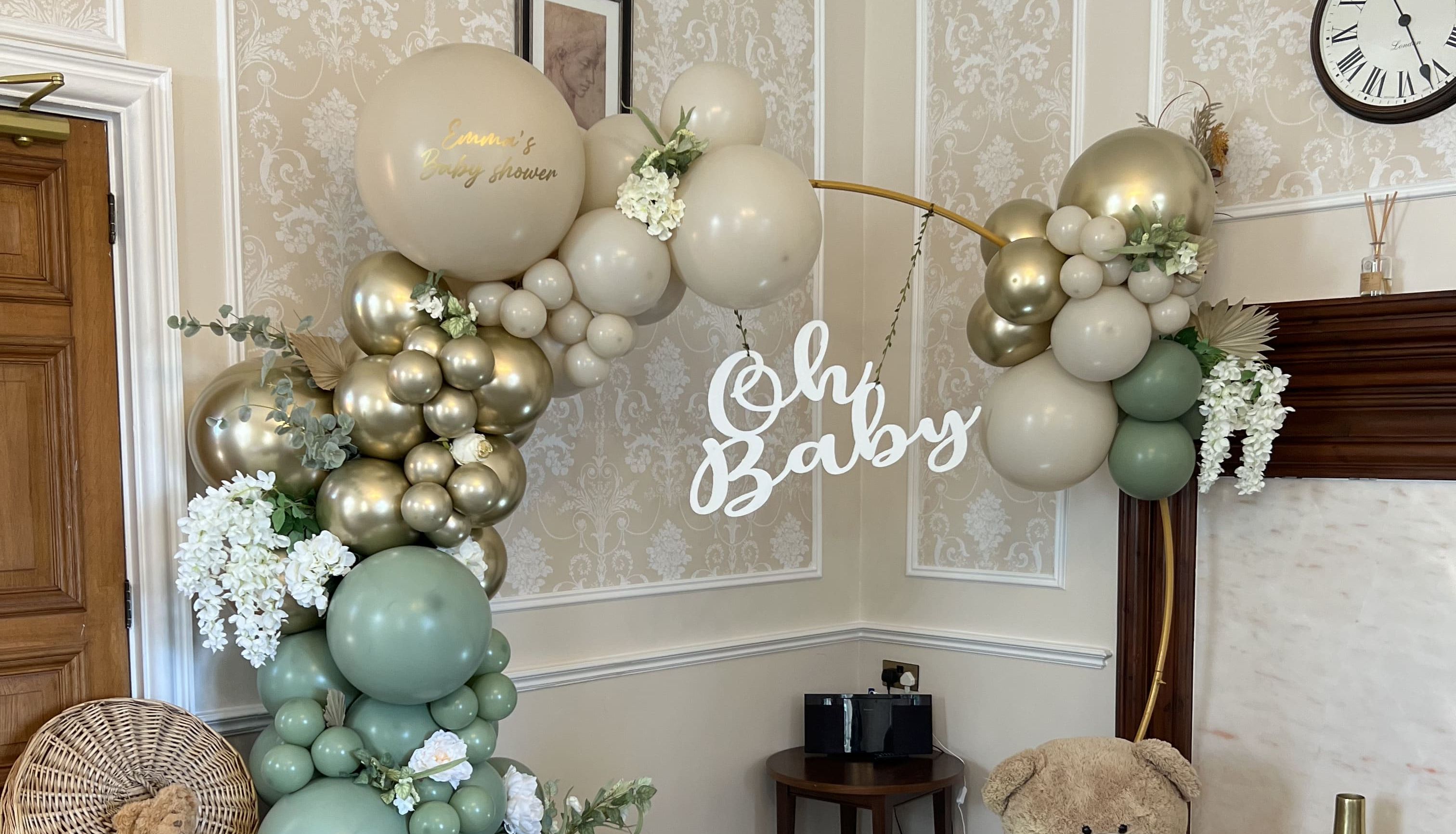 Elegant baby shower setup with pastel balloons, teddy bears, flowers, a wicker basket, and an 'Oh Baby' sign.