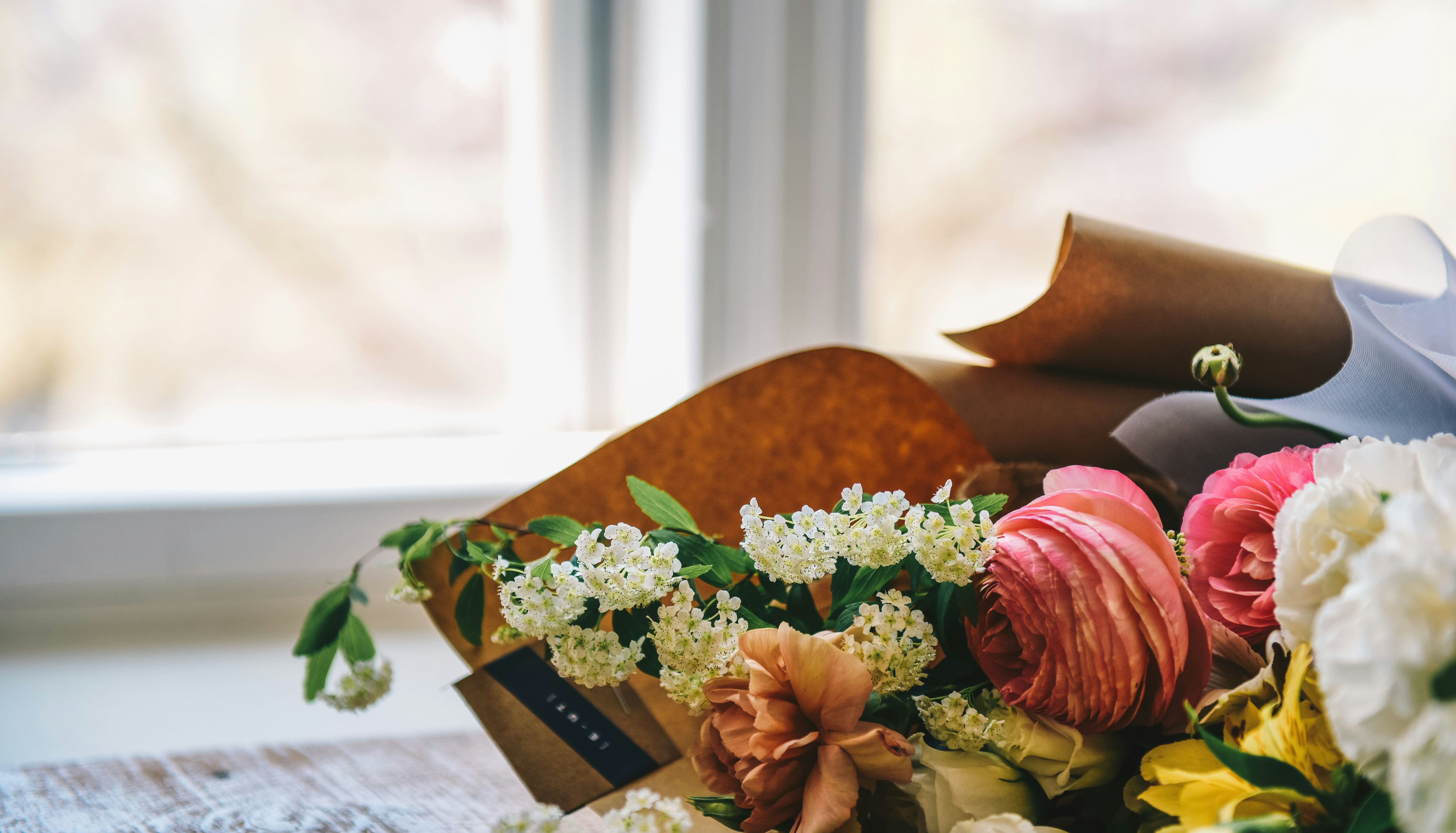 A close-up of a colorful bouquet of fresh flowers lying on a wooden table near a window.