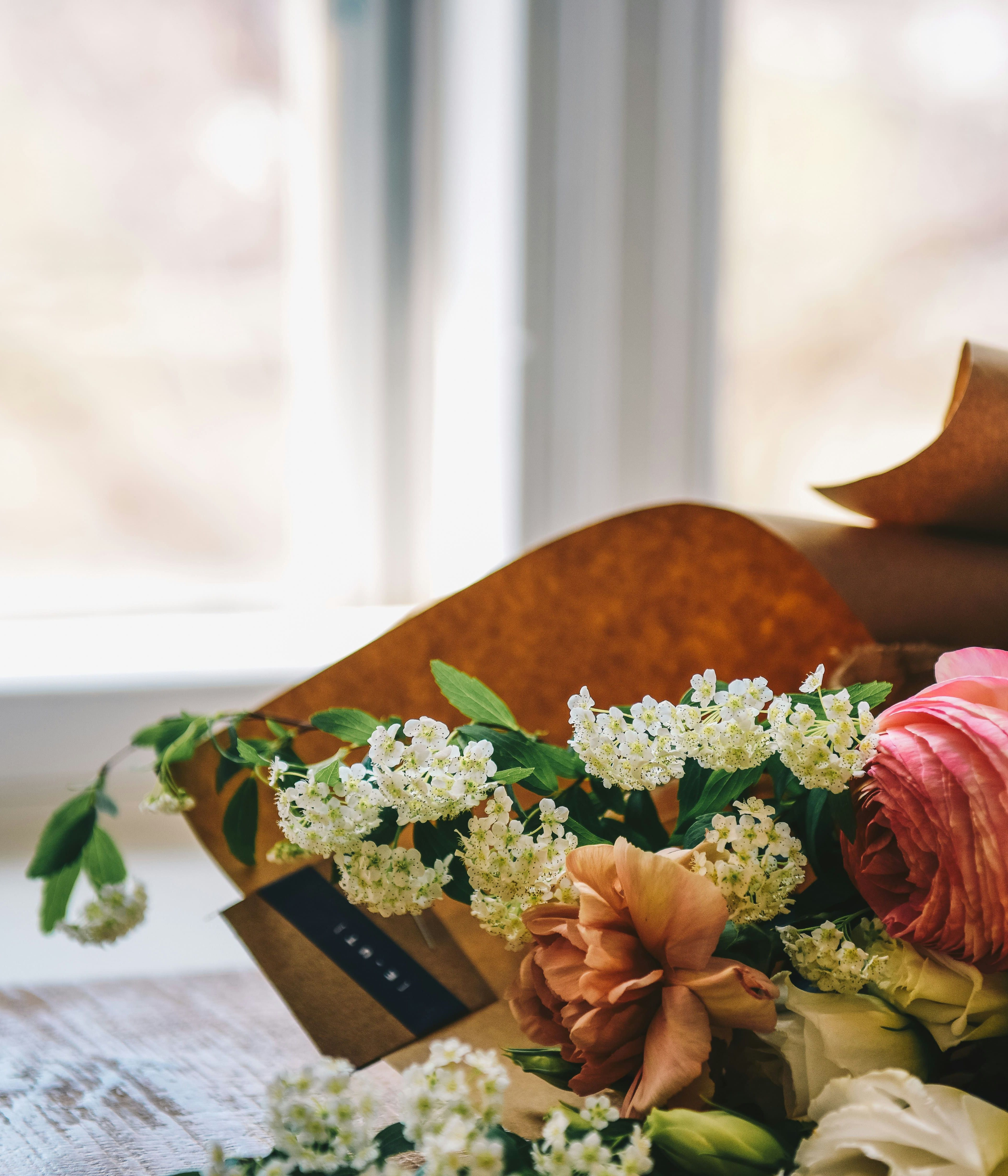 A close-up of a colorful bouquet of fresh flowers lying on a wooden table near a window.