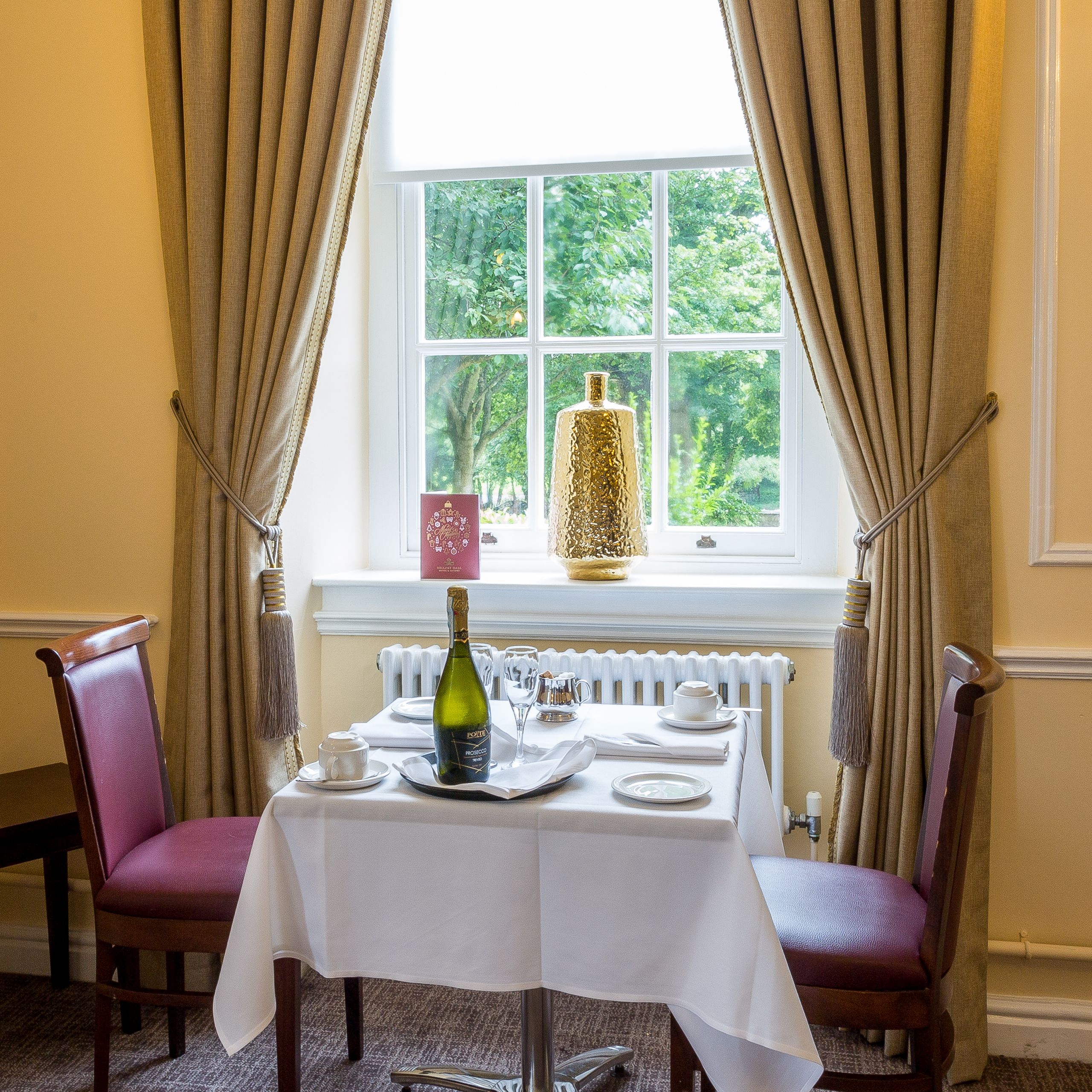 Elegant restaurant table set for two by a window with champagne bottle and tea cups.