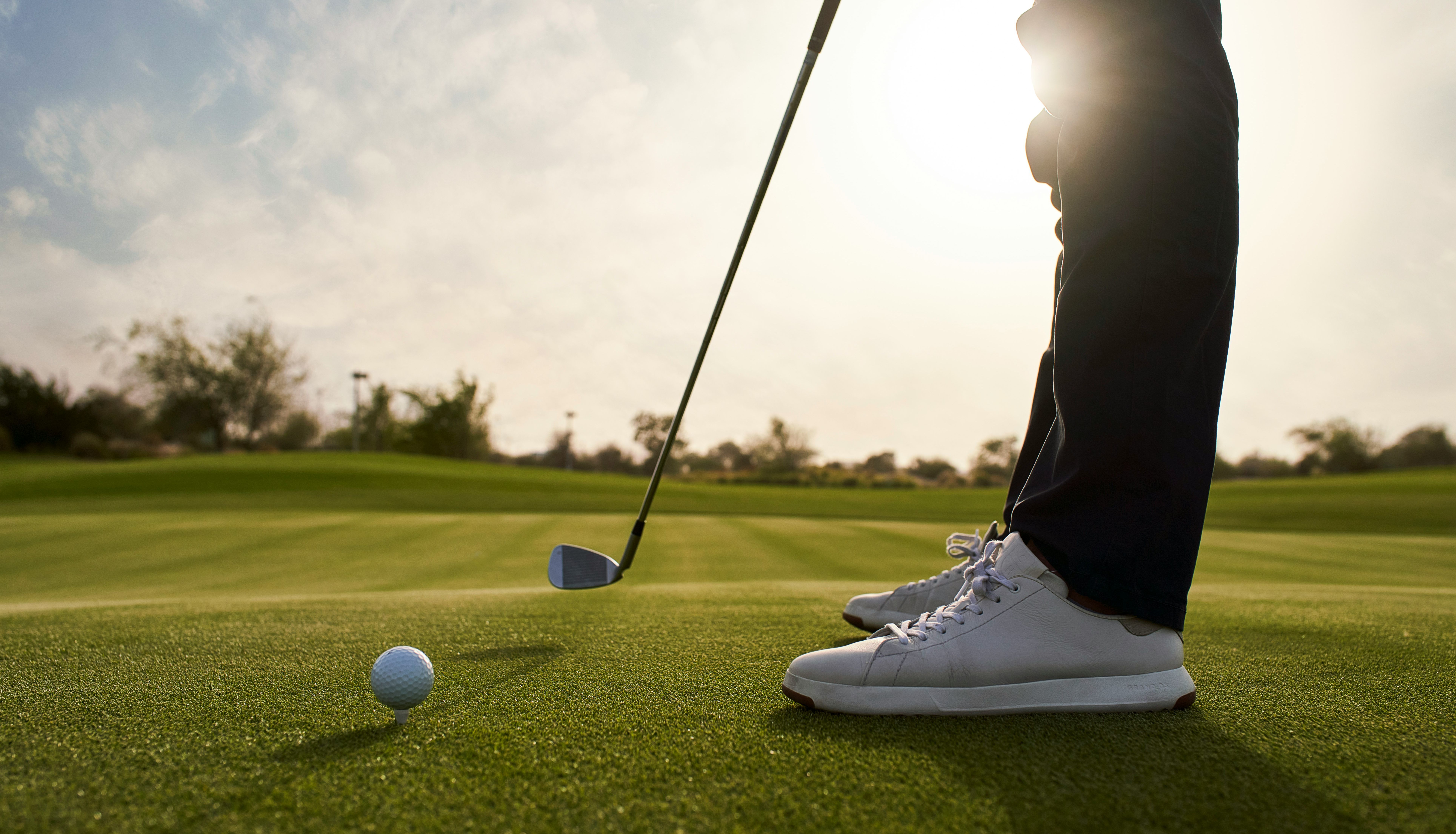 Golfer preparing to putt on a green with sunlight in the background