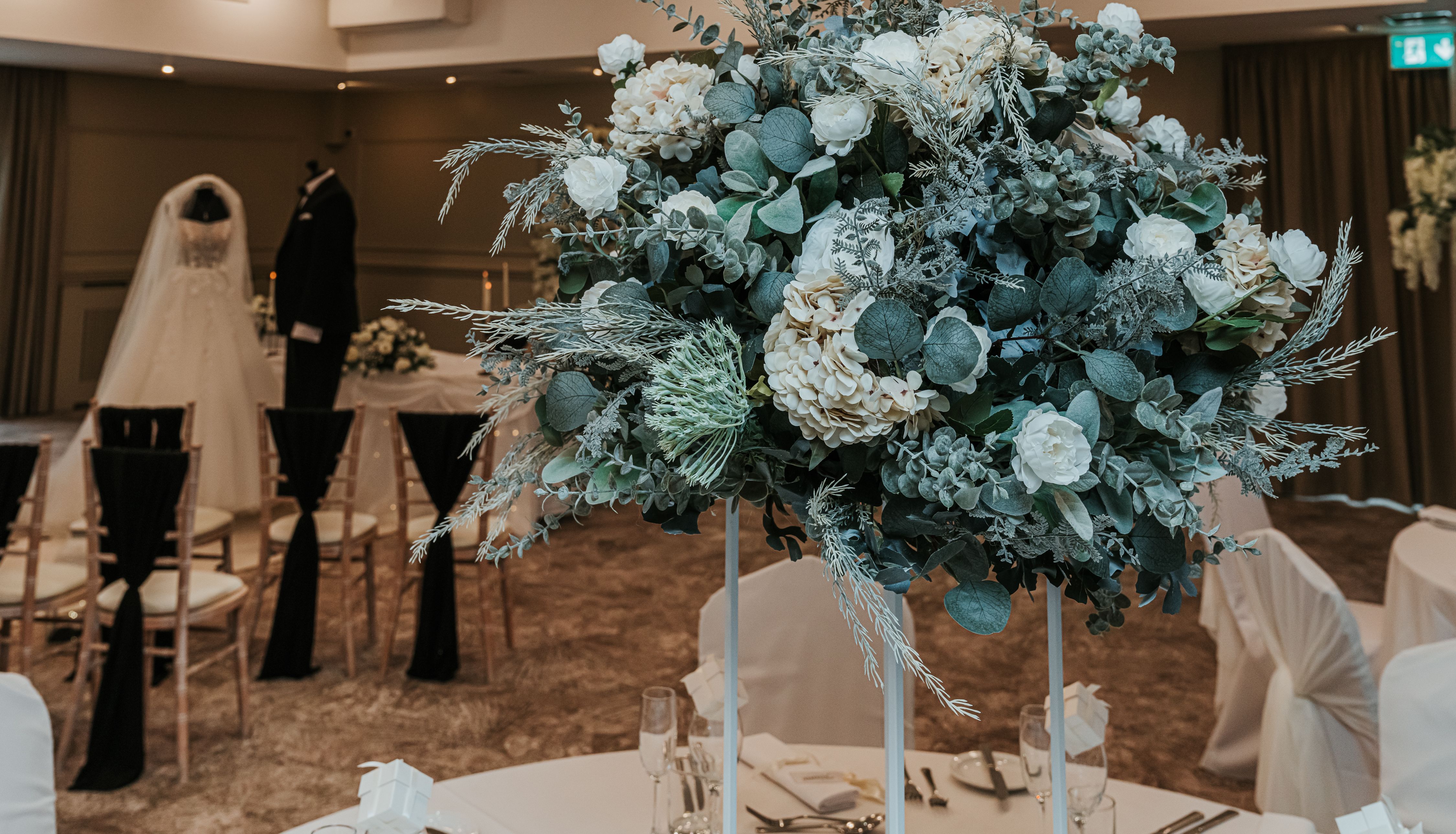 Elegant wedding reception room with floral centerpiece and mannequins dressed in bridal attire in the background