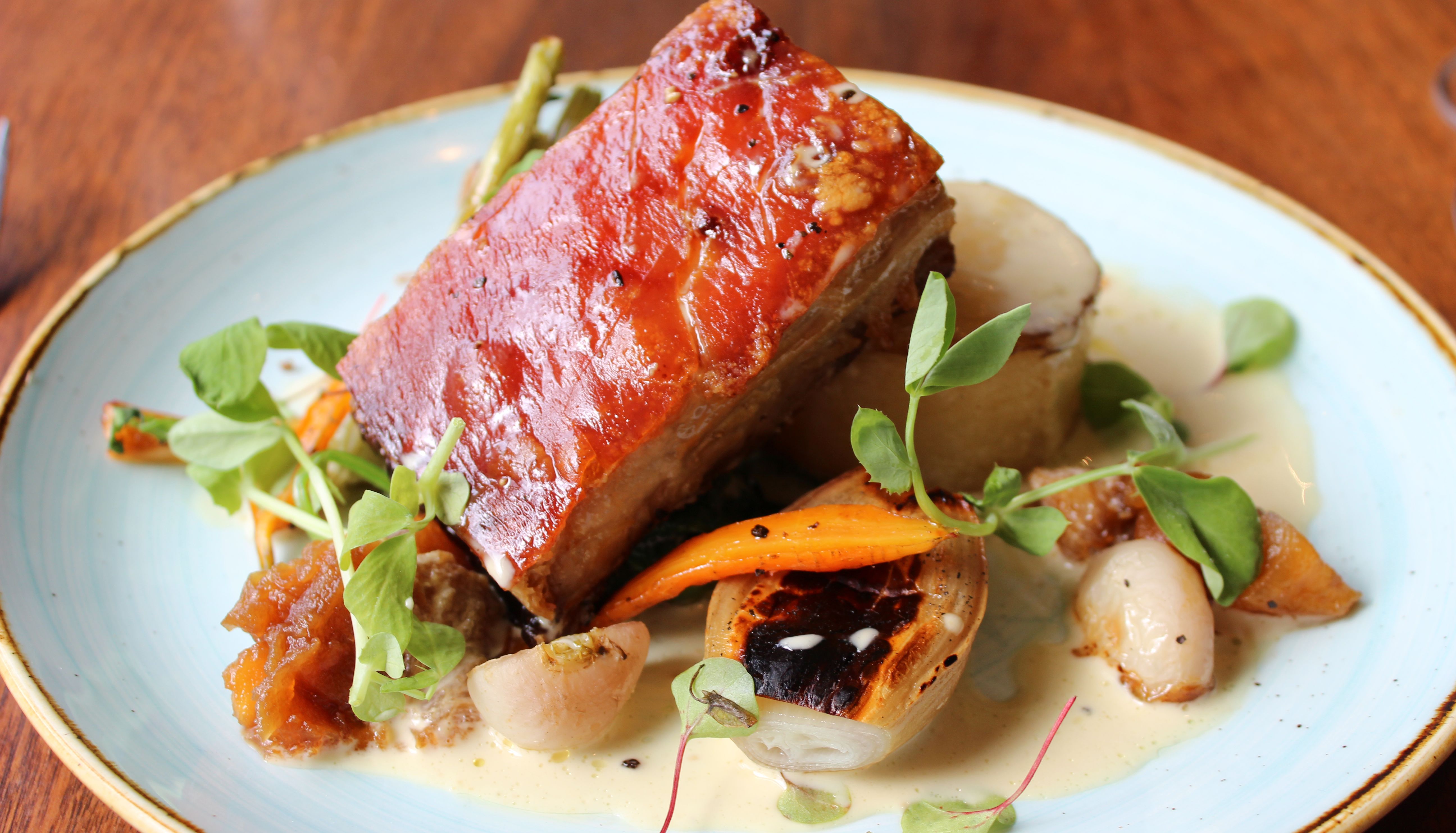 Plated dish with crispy pork belly, roasted vegetables, and garnish on a light blue plate