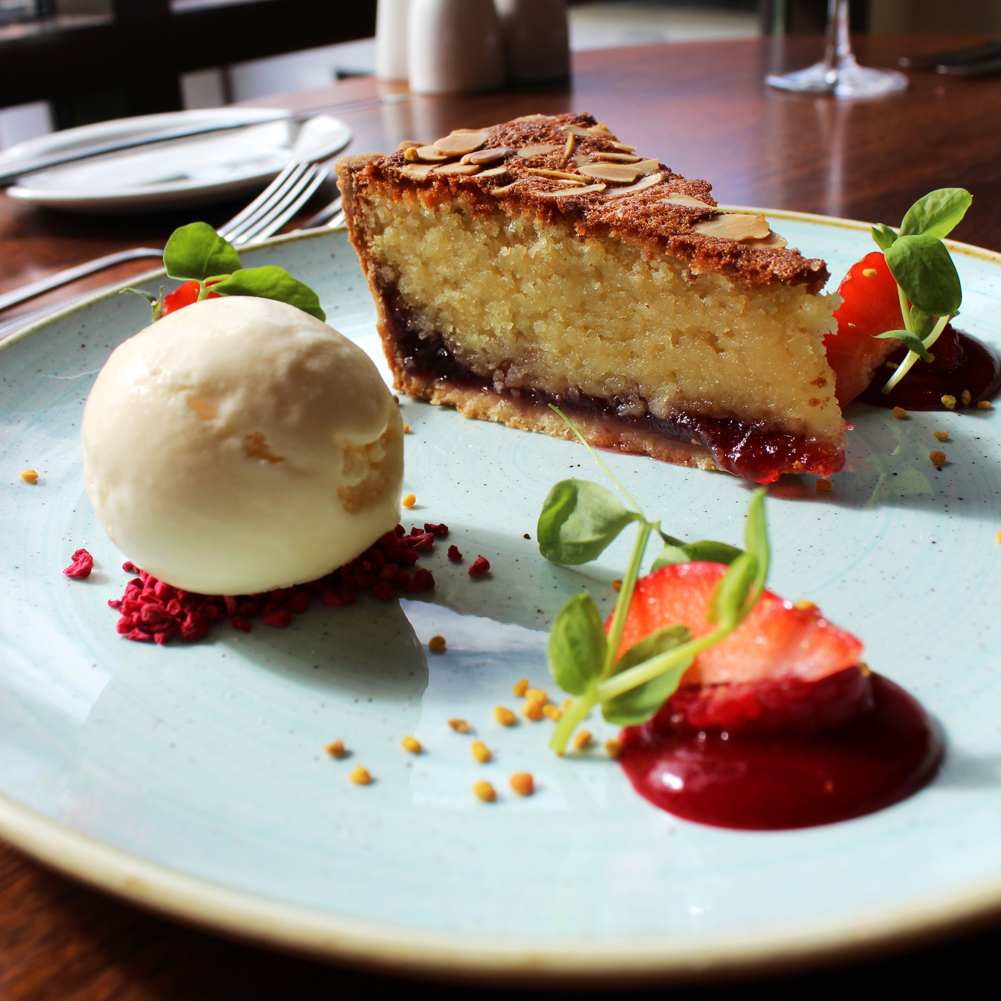 Slice of almond cake with a scoop of ice cream and strawberry garnish on a blue plate