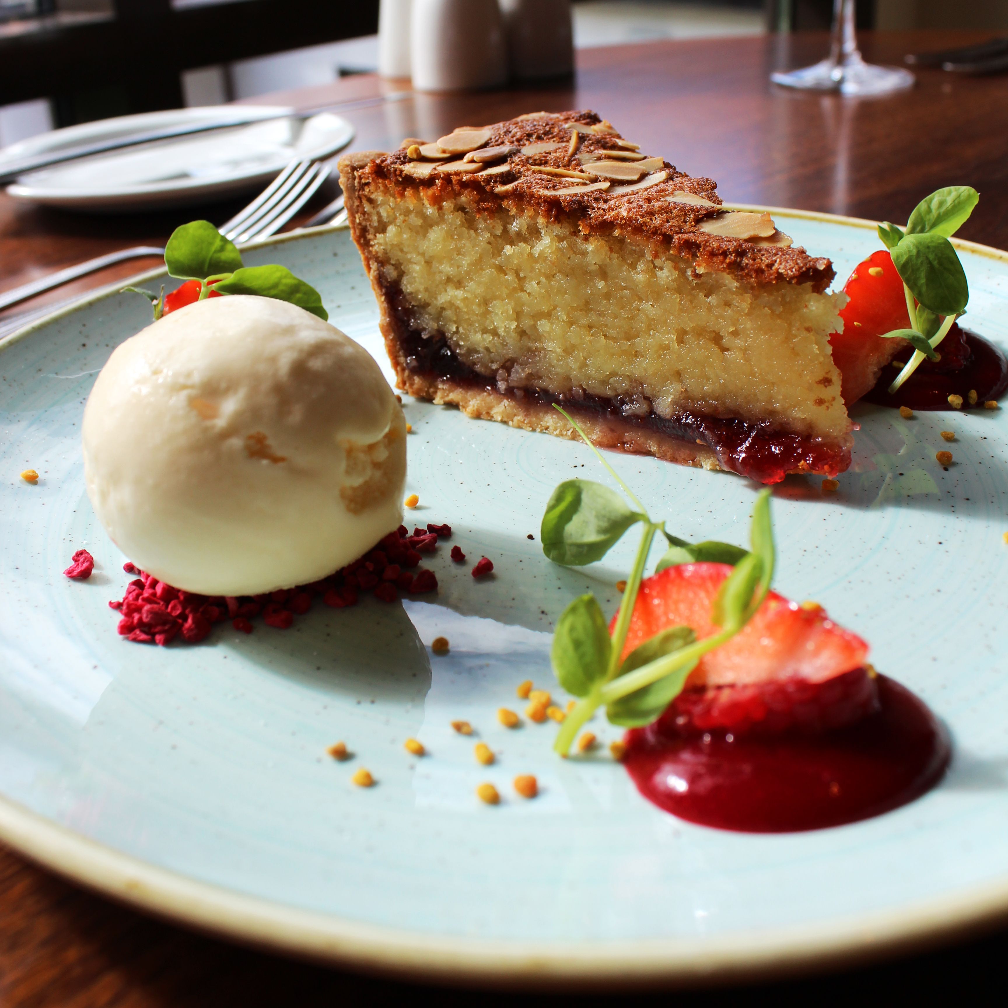 Slice of almond cake with a scoop of ice cream and strawberry garnish on a blue plate