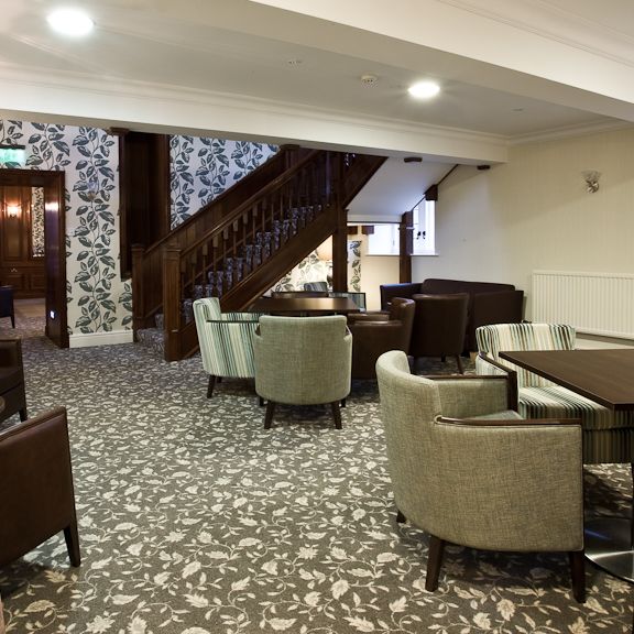 Modern lounge area with armchairs, tables, patterned carpet, and staircase