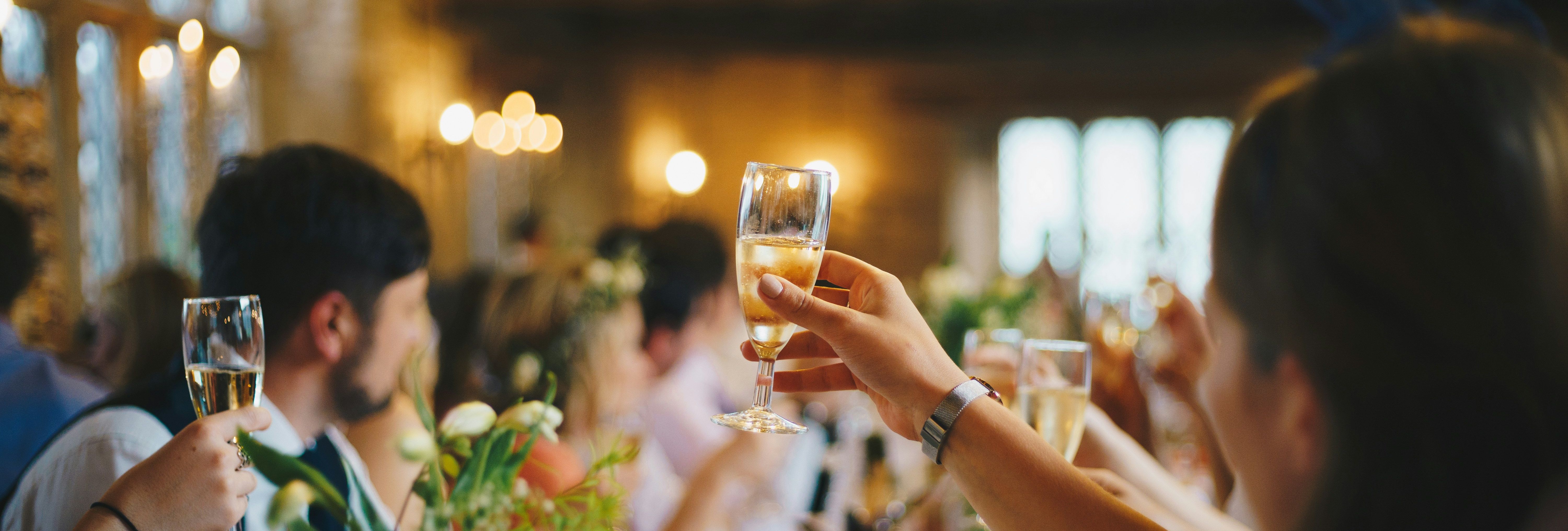 People raising champagne glasses in a toast at a festive gathering with warm string lights overhead.