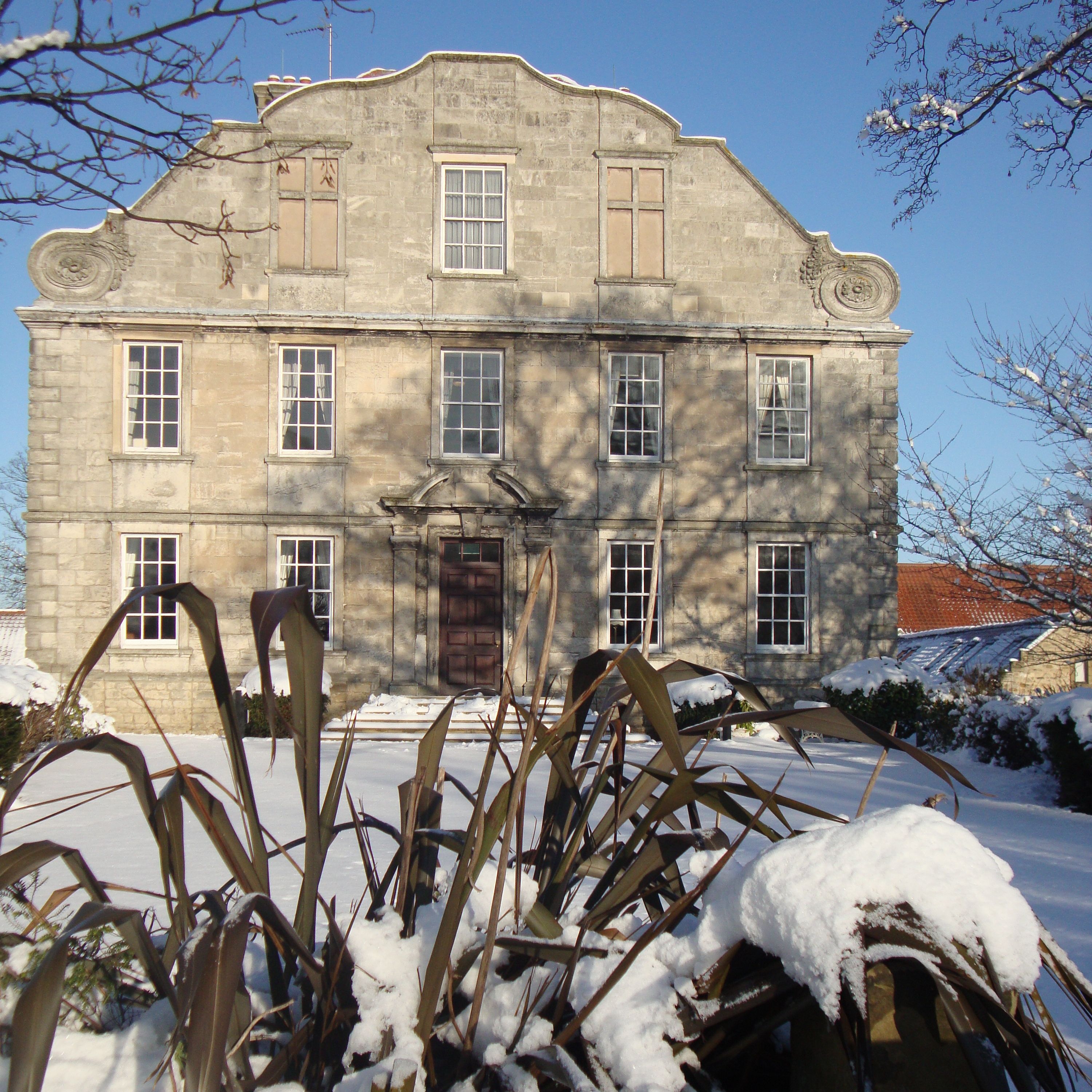 Old stone building with symmetrical windows and a decorative roofline, viewed on a snowy winter day.