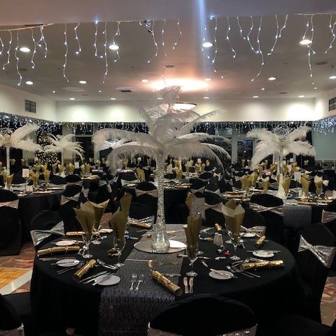 Elegant banquet hall with black and gold decor, set tables, and white feather centerpieces