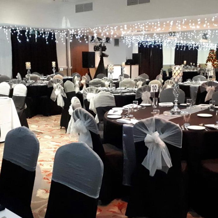 Elegant banquet hall set up for an event with black and white decorated tables and chairs under string lights.
