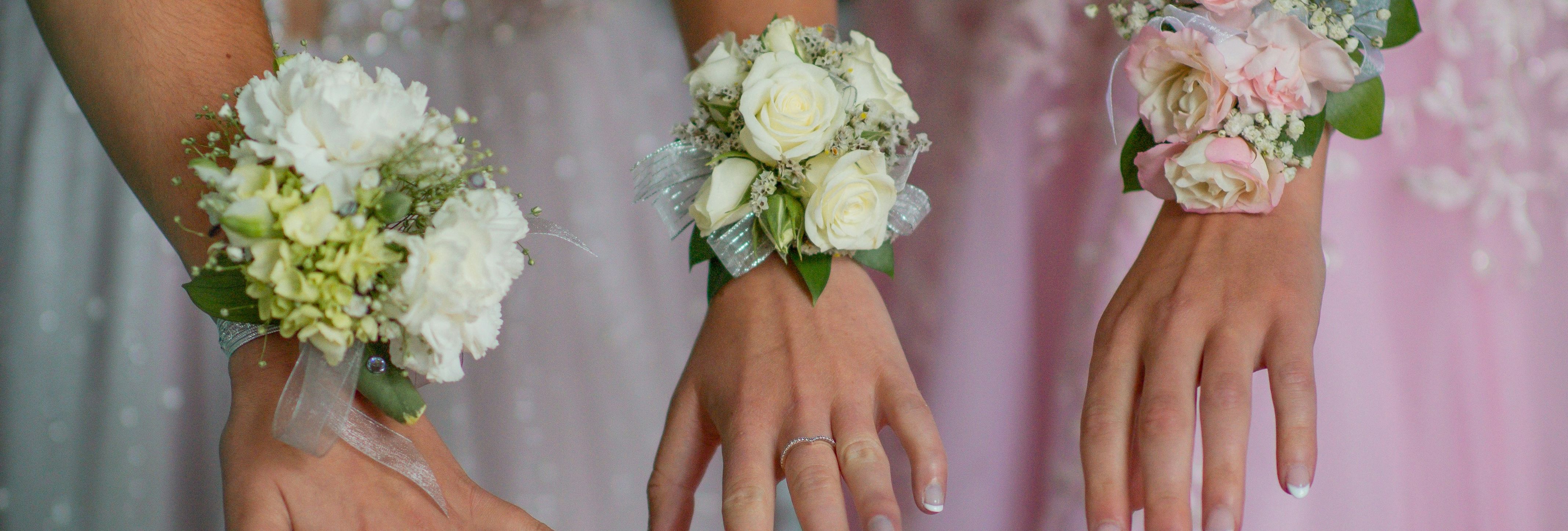 Three hands wearing floral corsages, each hand belonging to a person in a formal dress.
