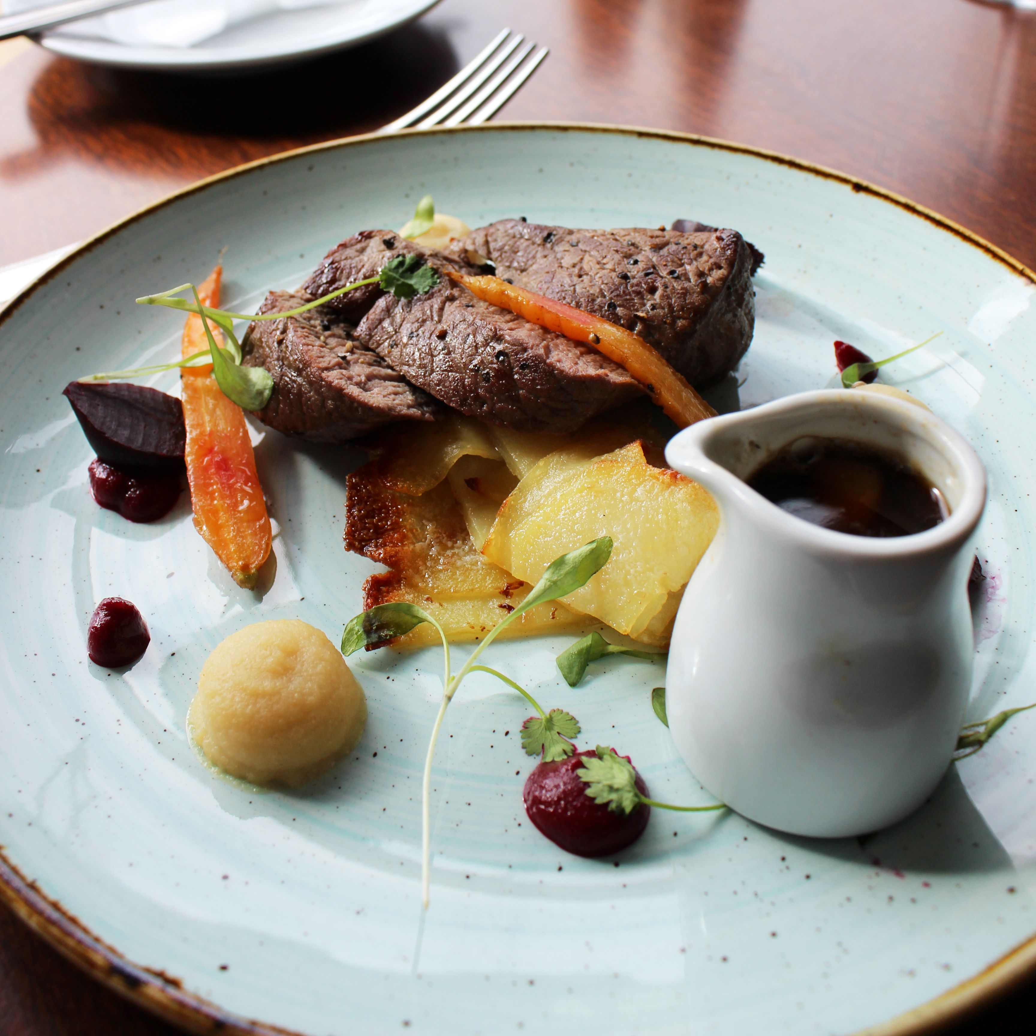 Gourmet steak dish served with vegetables, sauce, and garnishes on a plate in a restaurant setting