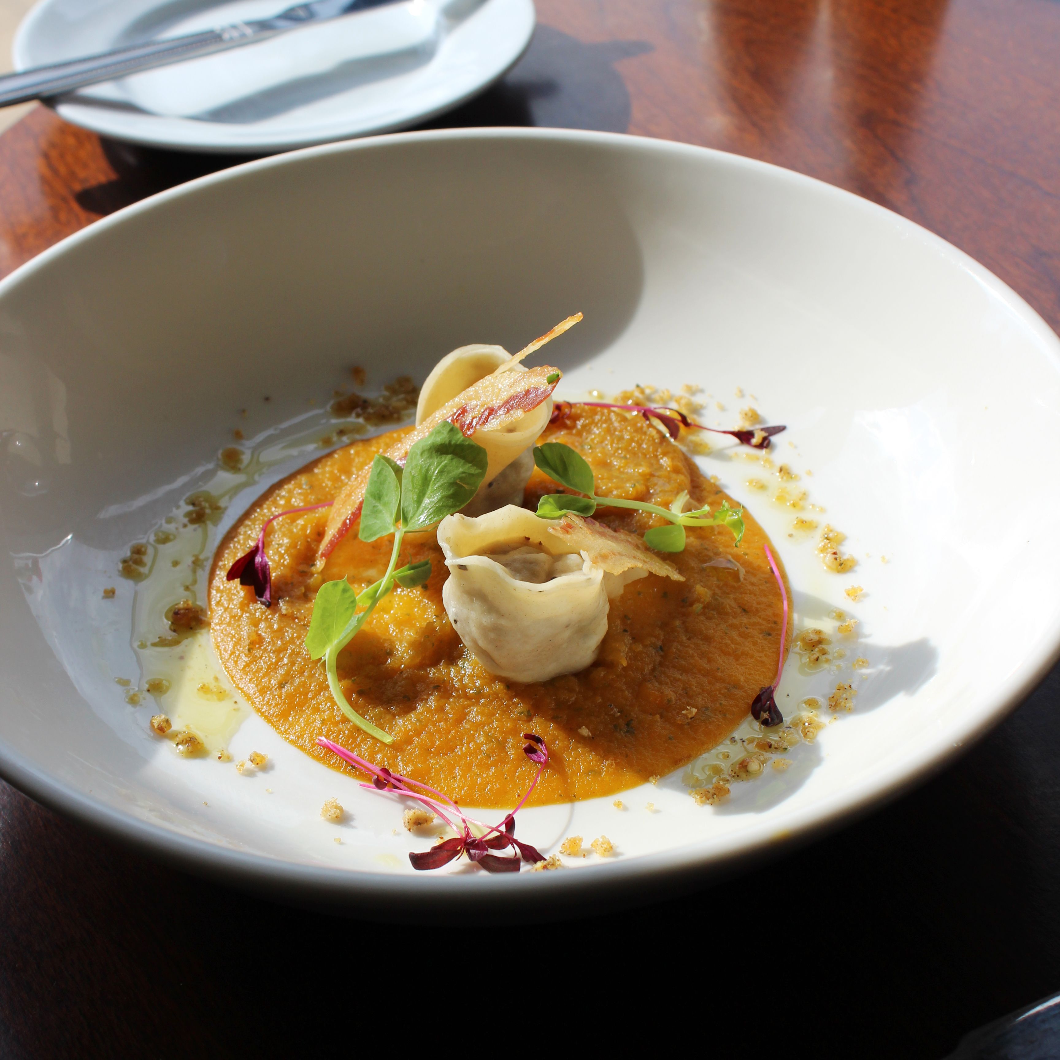 Plated gourmet dish with dumplings on a creamy orange sauce, garnished with microgreens and edible flowers.