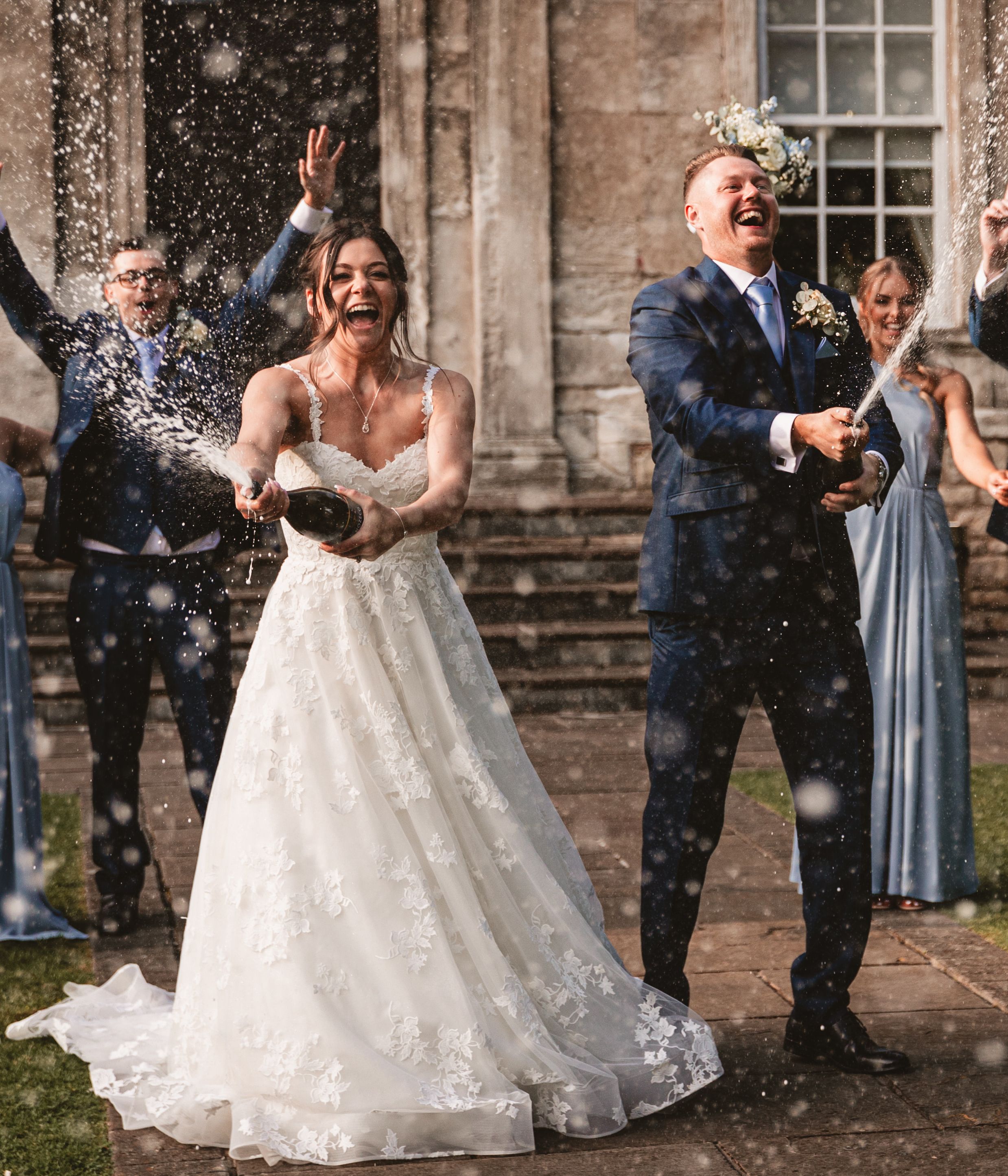 Bride and groom spraying champagne with their wedding party celebrating outdoors.