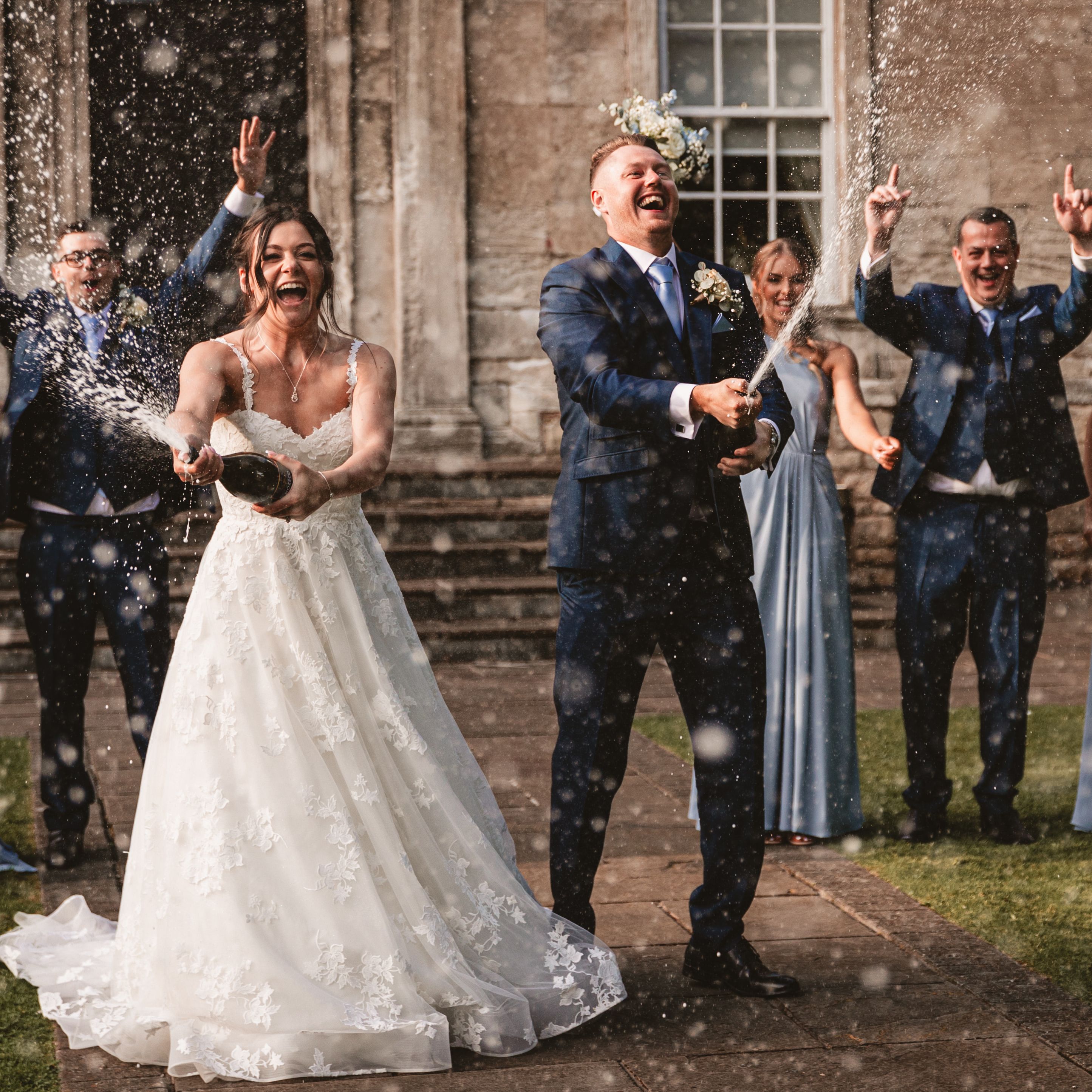 Bride and groom spraying champagne with their wedding party celebrating outdoors.