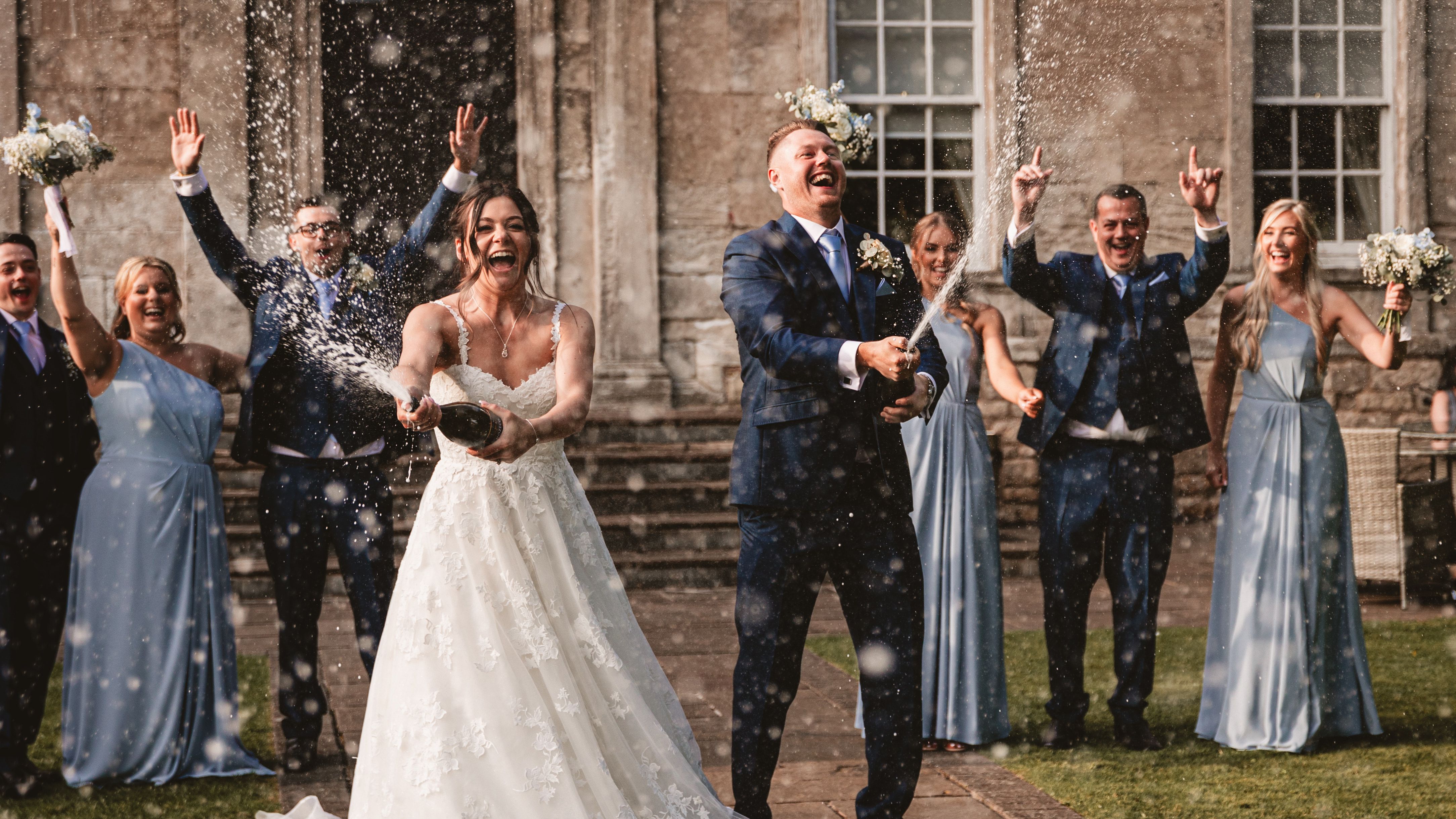 Bride and groom spraying champagne with their wedding party celebrating outdoors.