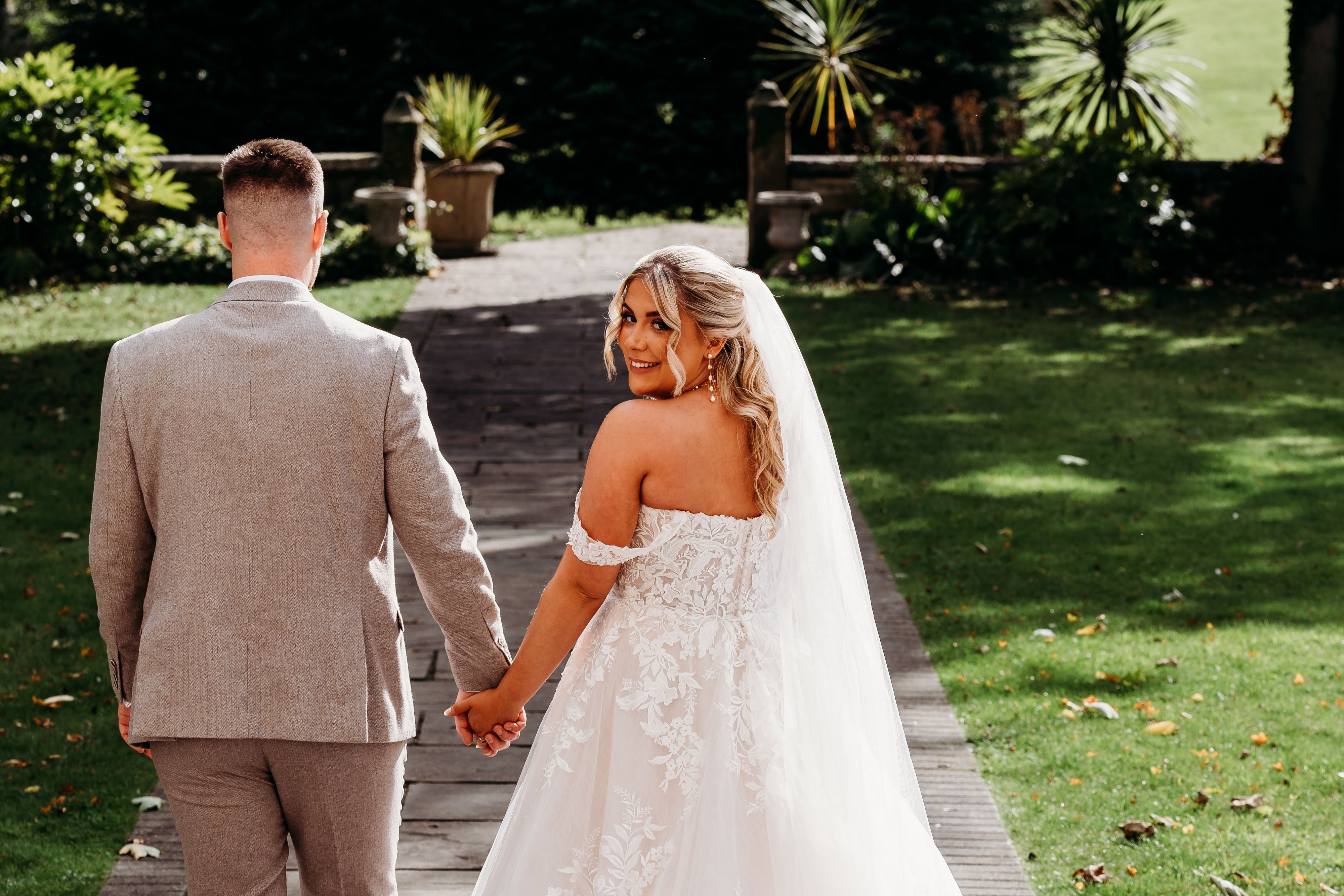 Bride and groom holding hands while walking outdoors on a stone path, with the bride looking back and smiling.