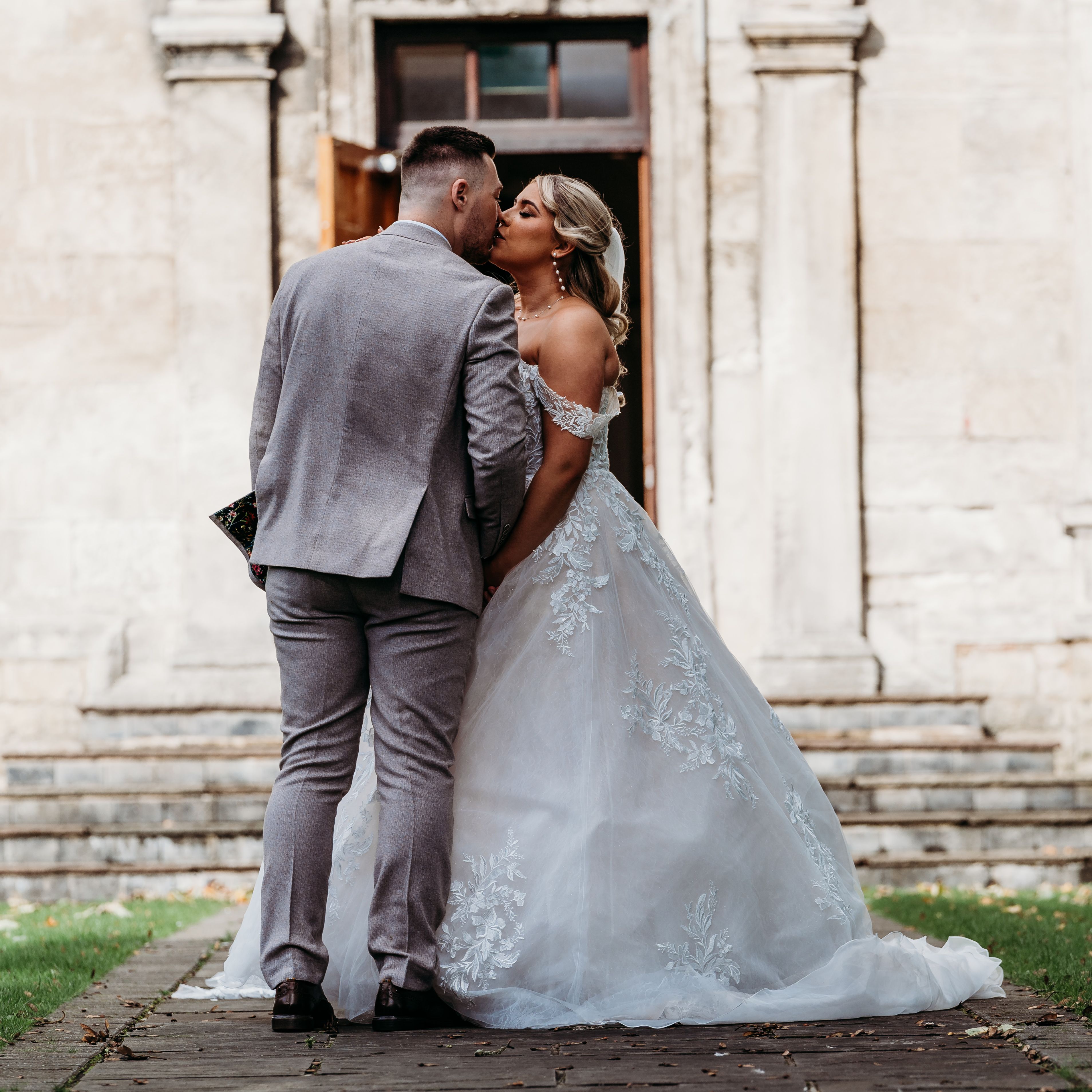 Bride and groom share a kiss outside a stone building on their wedding day.