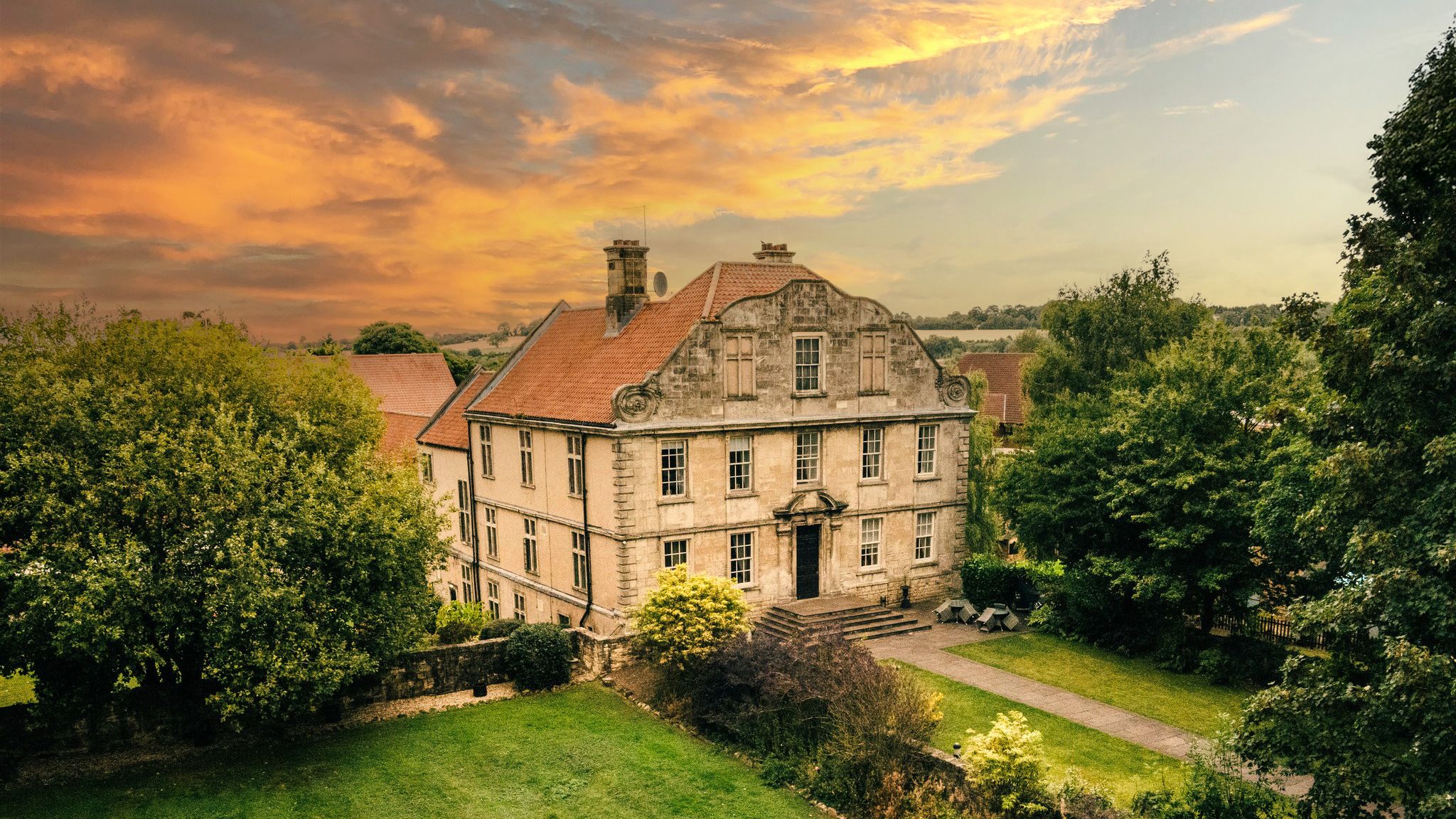 Aerial view of a bride and groom walking on a large lawn in front of a grand historic building during sunset.