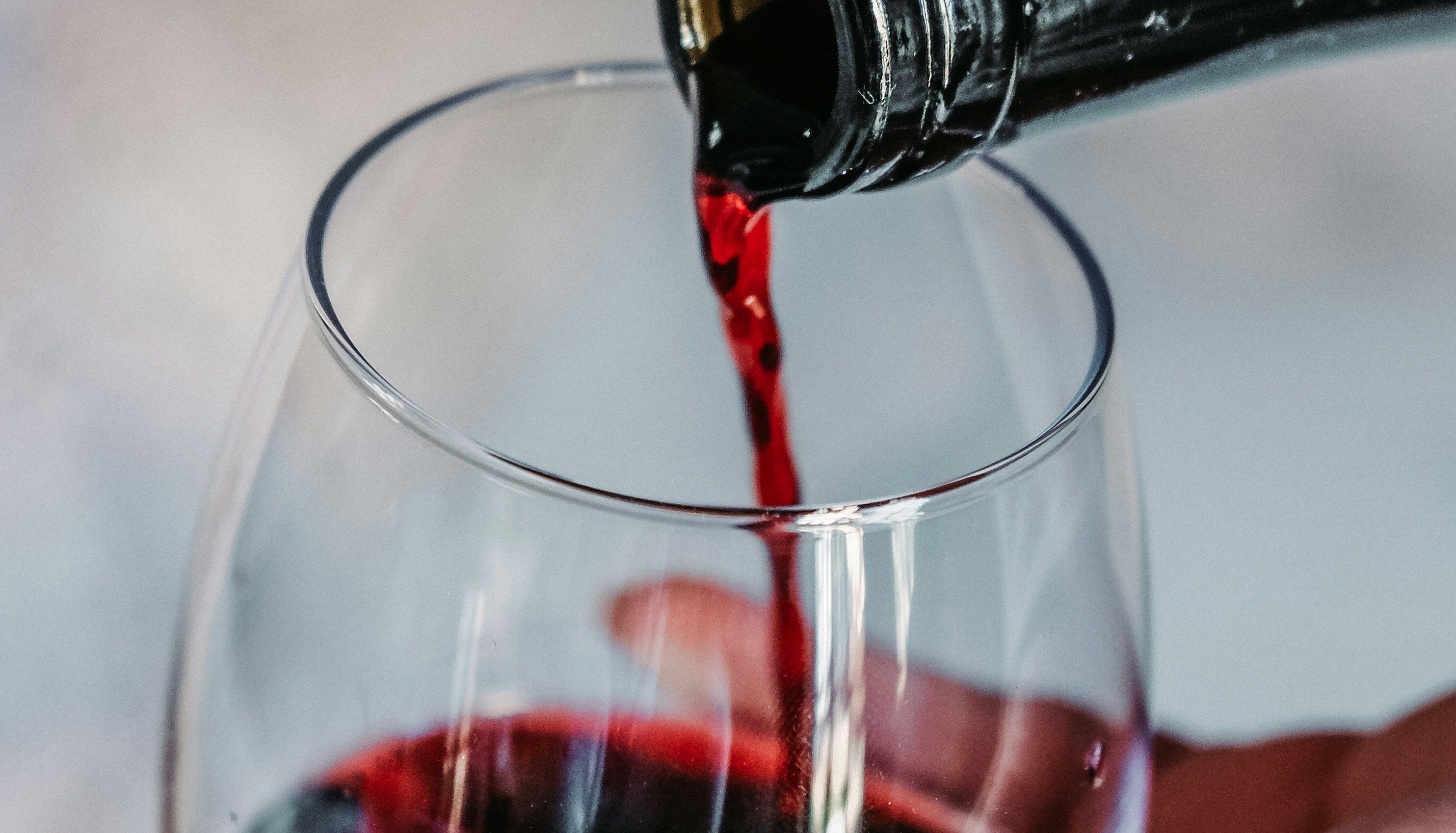 Red wine being poured from a bottle into a glass held by a hand