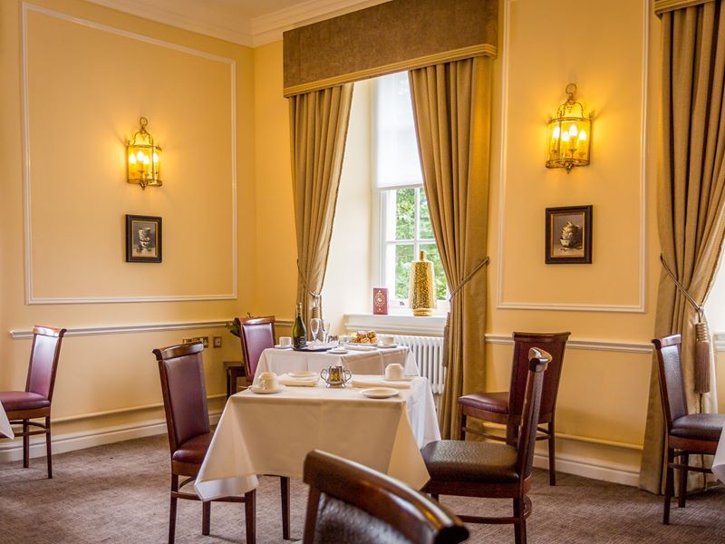 Elegant dining room with tables set for meal, large windows with curtains, and warm lighting