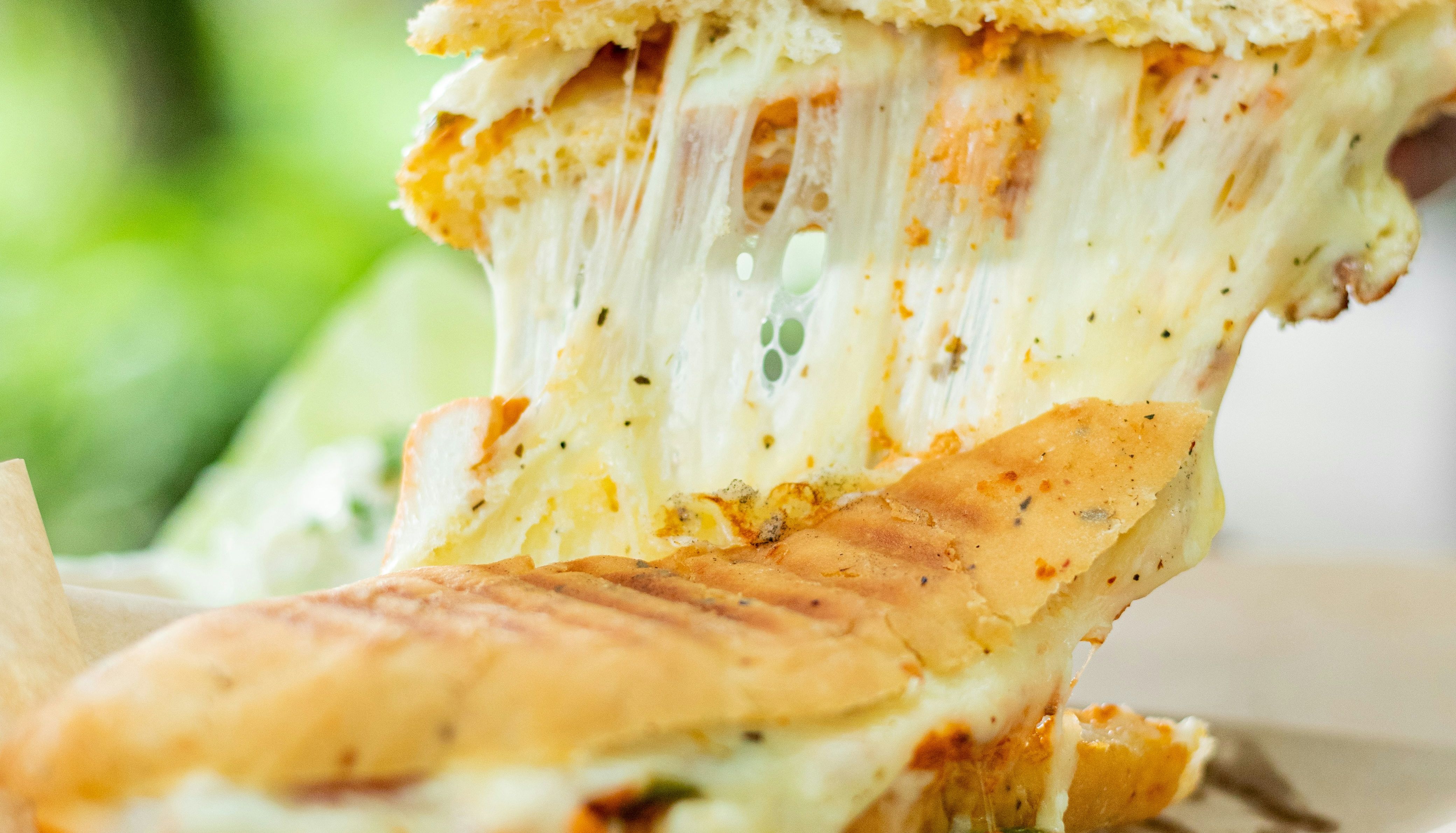 Hand pulling apart a cheesy panini sandwich with melted cheese stretching