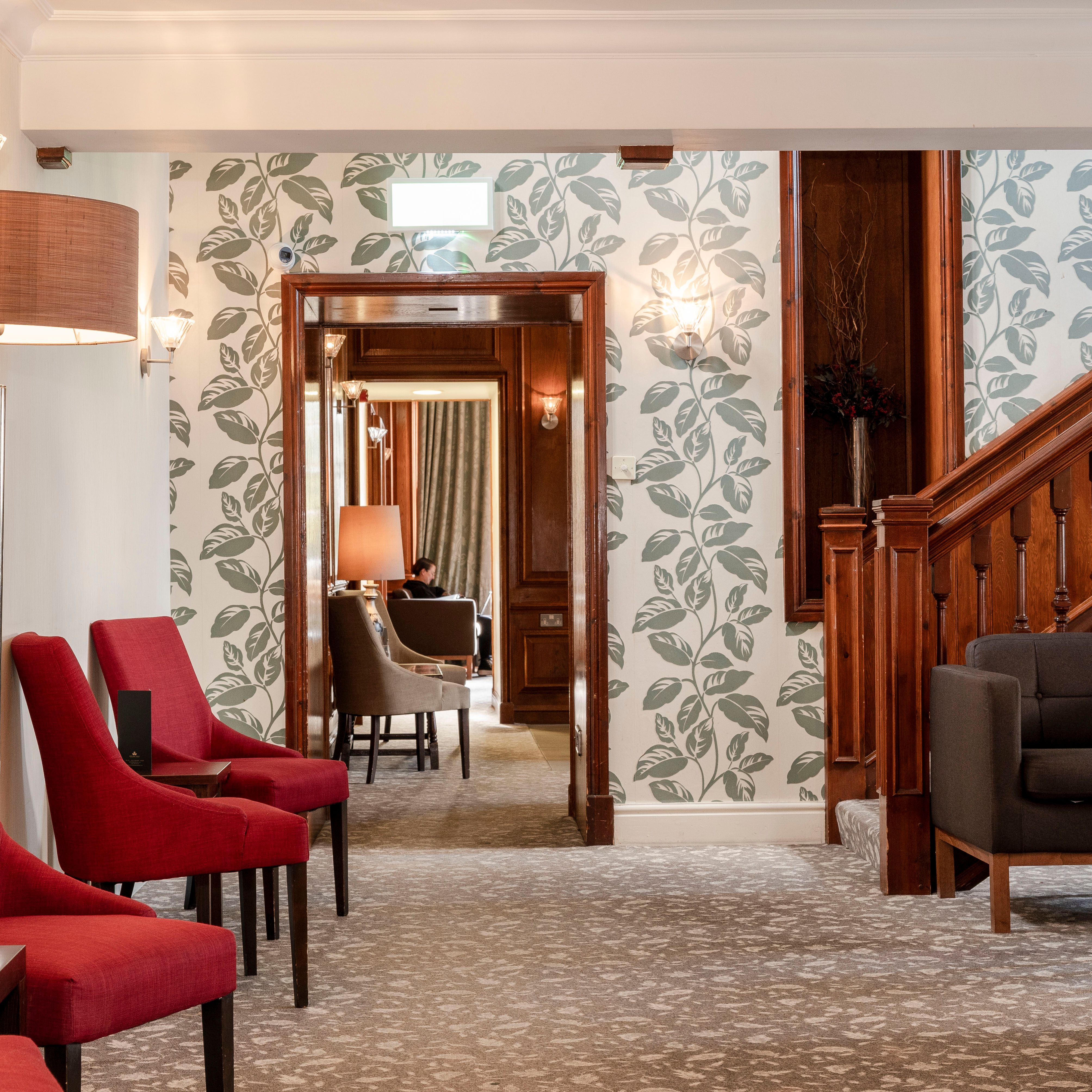 Cozy hotel lounge area with red chairs, patterned wallpaper, and wooden staircase.