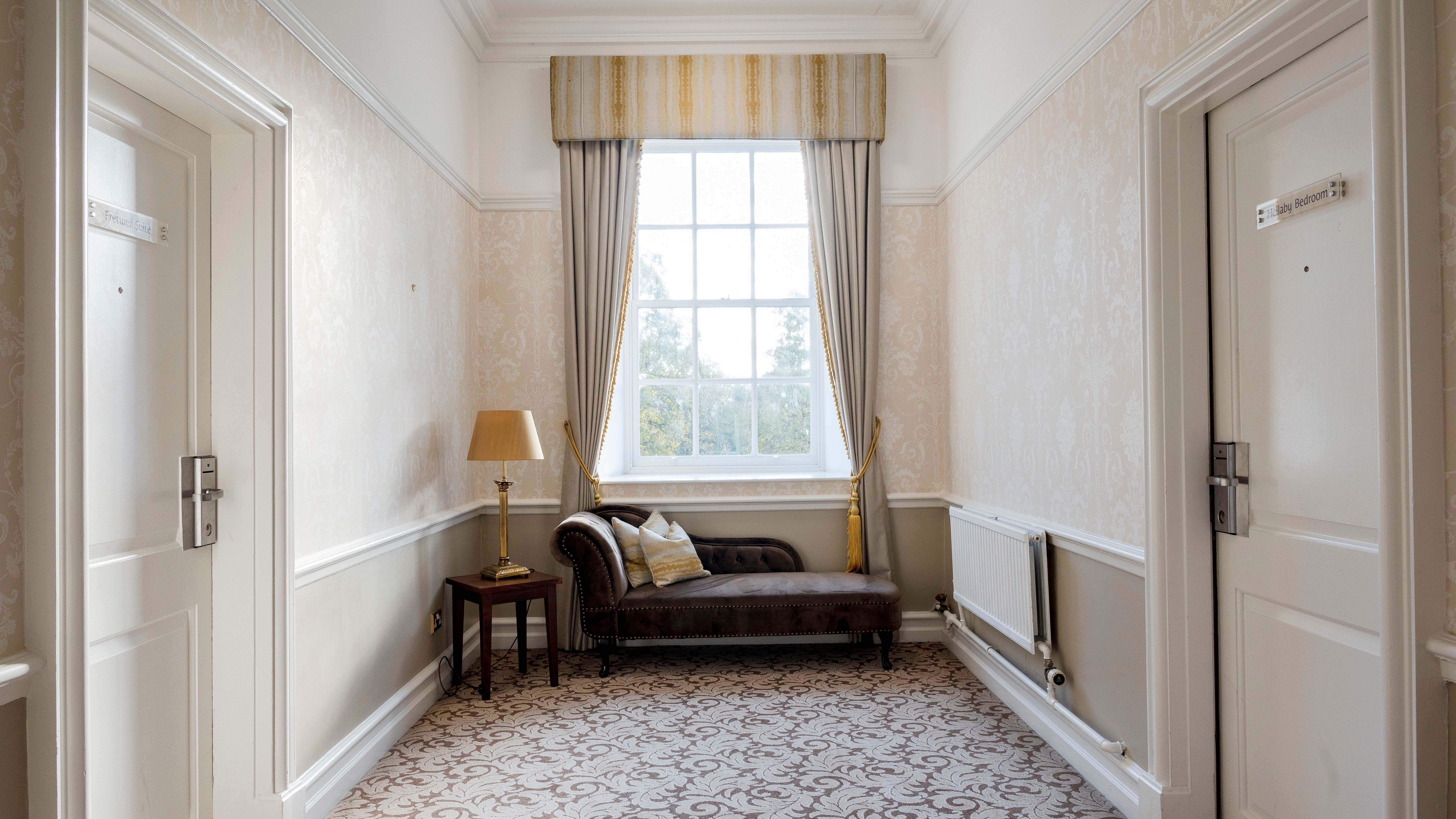 Elegant hallway with two doors, a window, a chaise lounge, lamp and side table