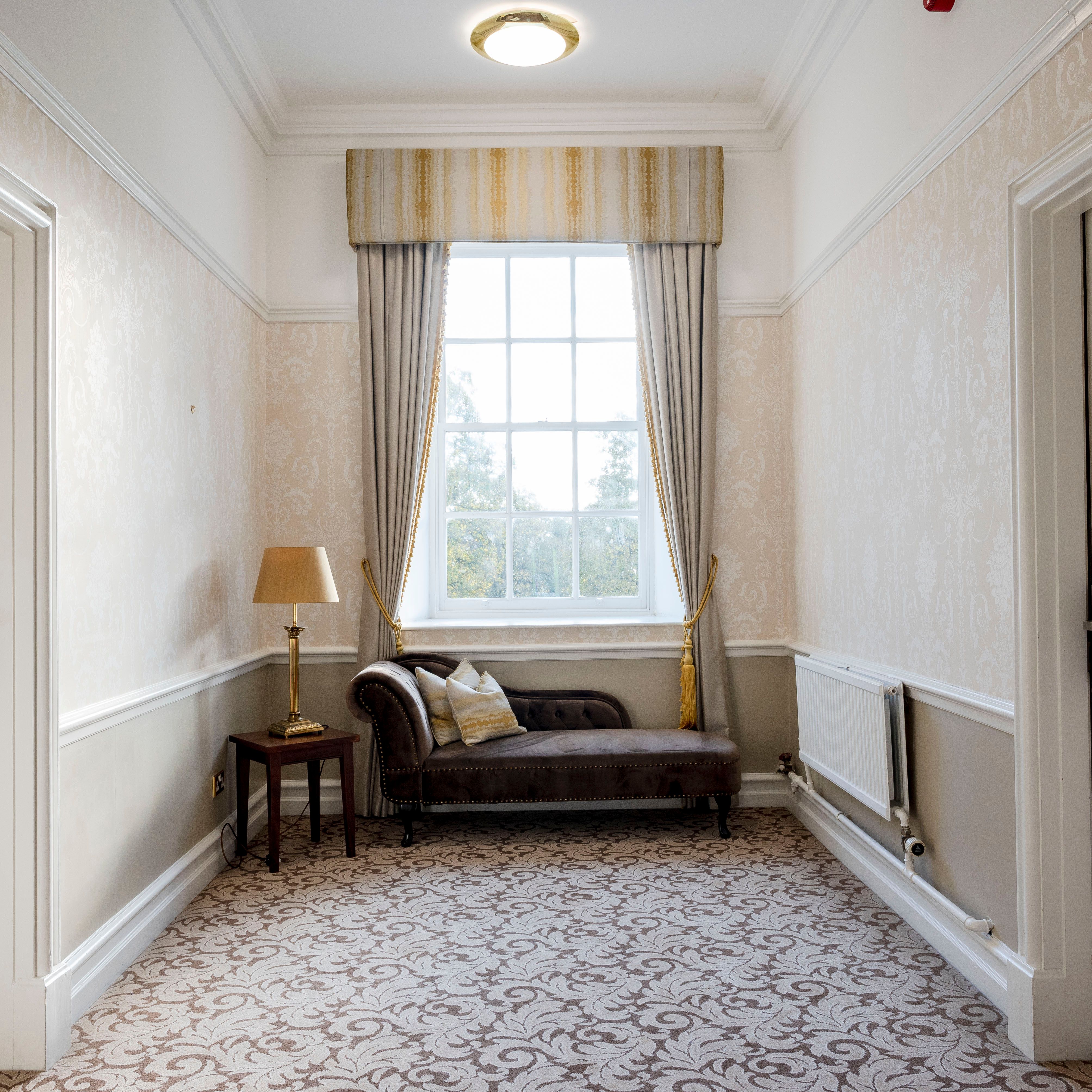 Elegant hallway with two doors, a window, a chaise lounge, lamp and side table